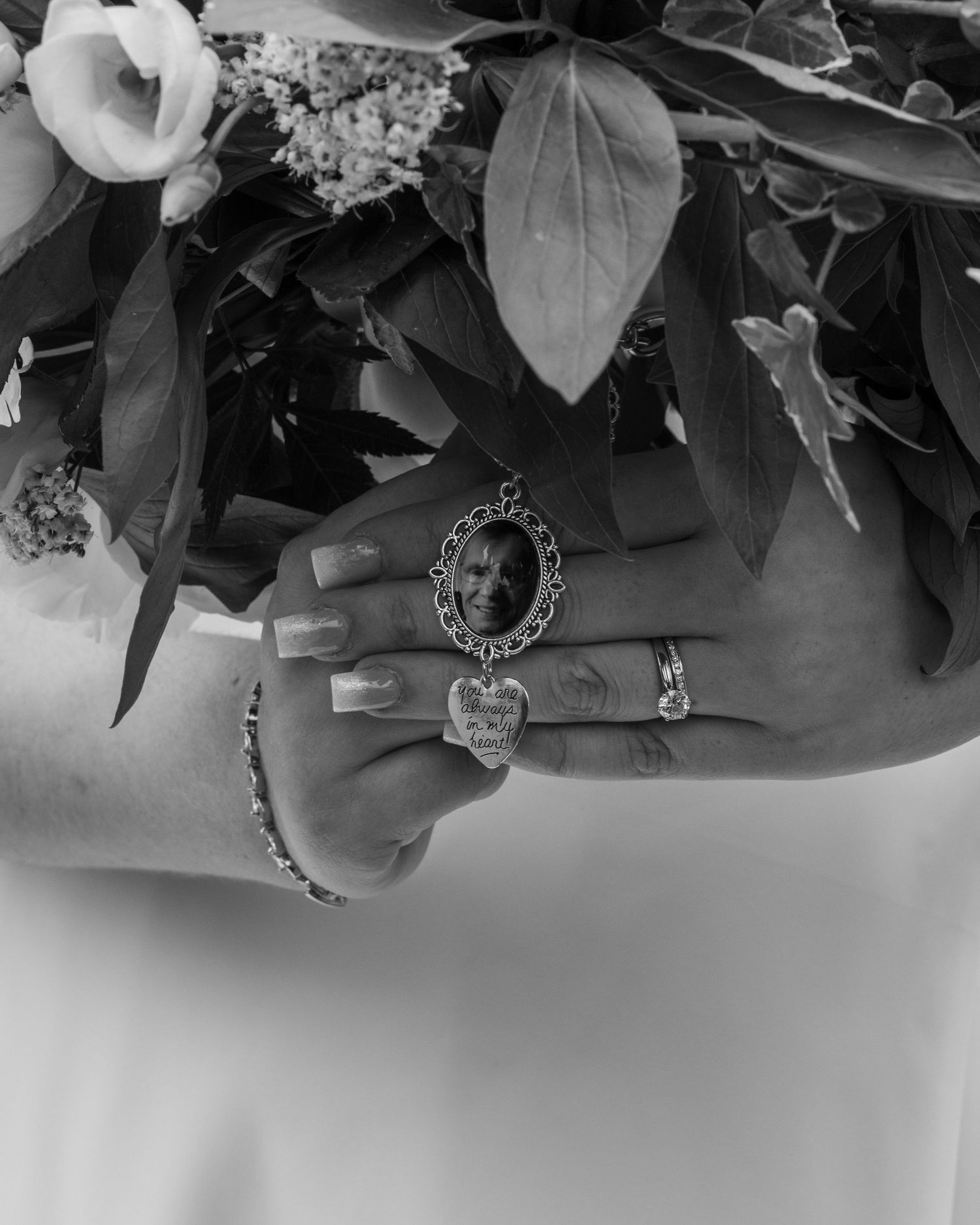 Close-up of white roses and delicate foliage in the bride's wedding bouquet and a detail of a memorial brooch.