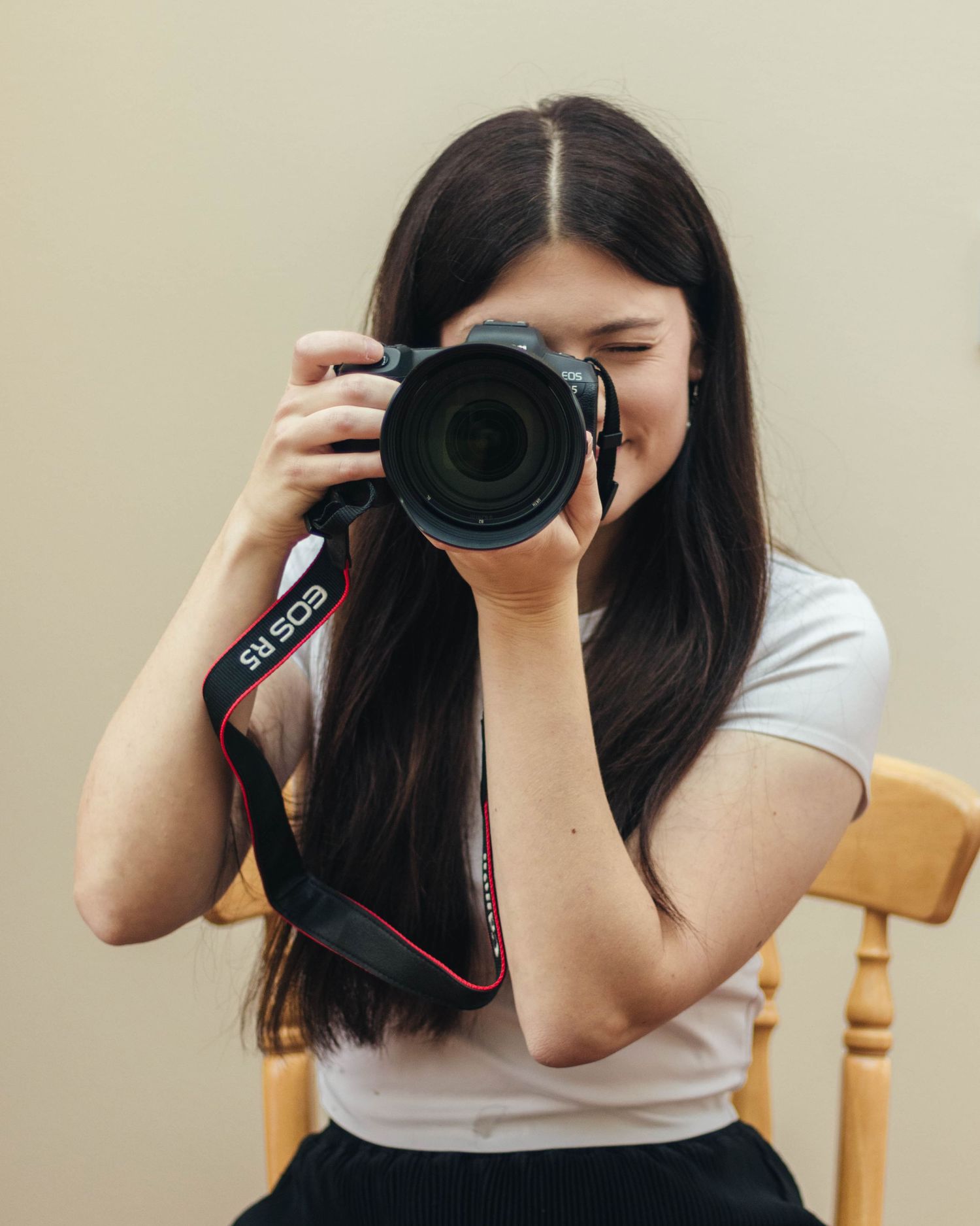 A girl holding a camera pointing towards the camera, as if she was taking a photograph.