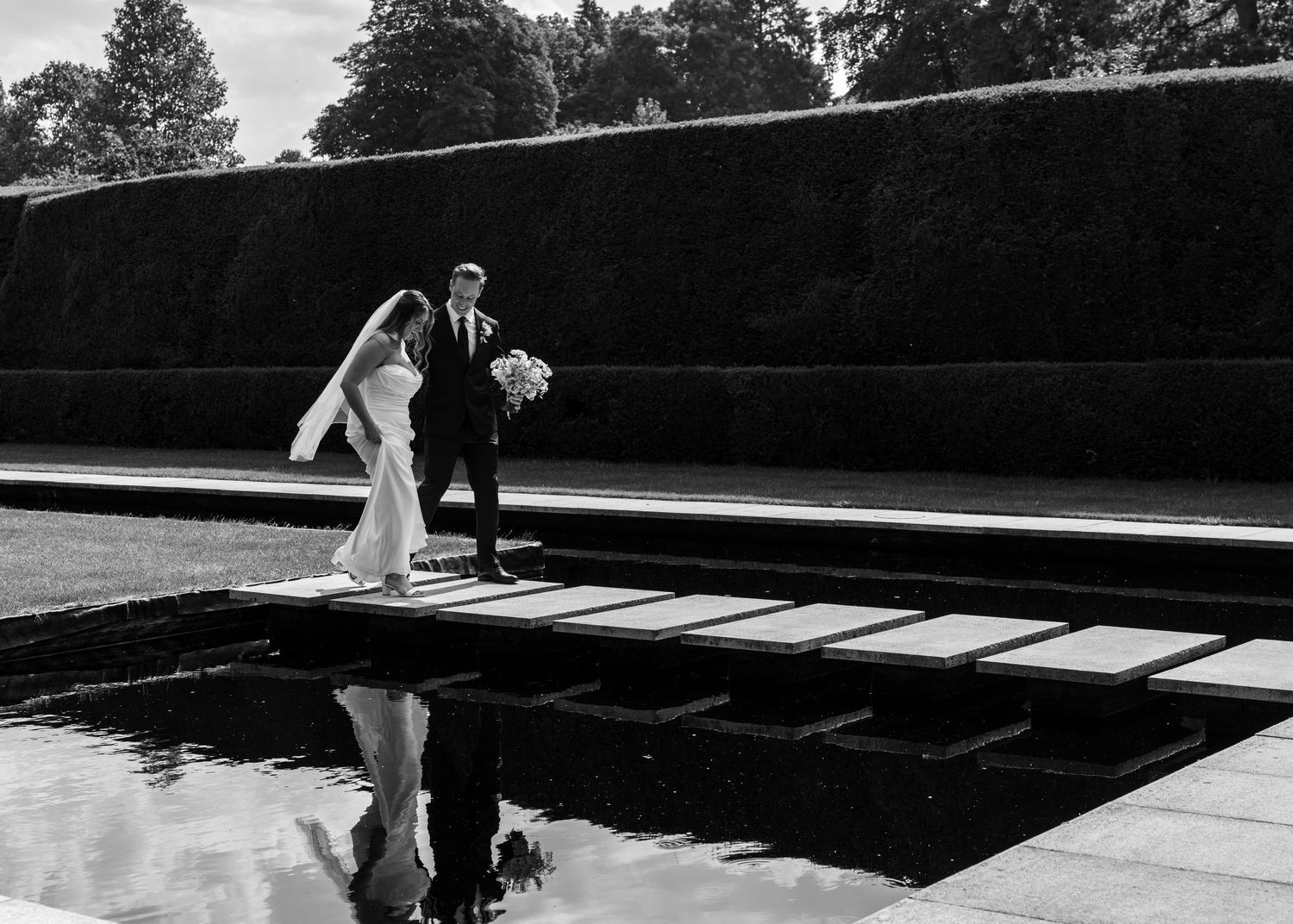 Bride and groom crossing stepping stones at Kiftsgate Court Gardens