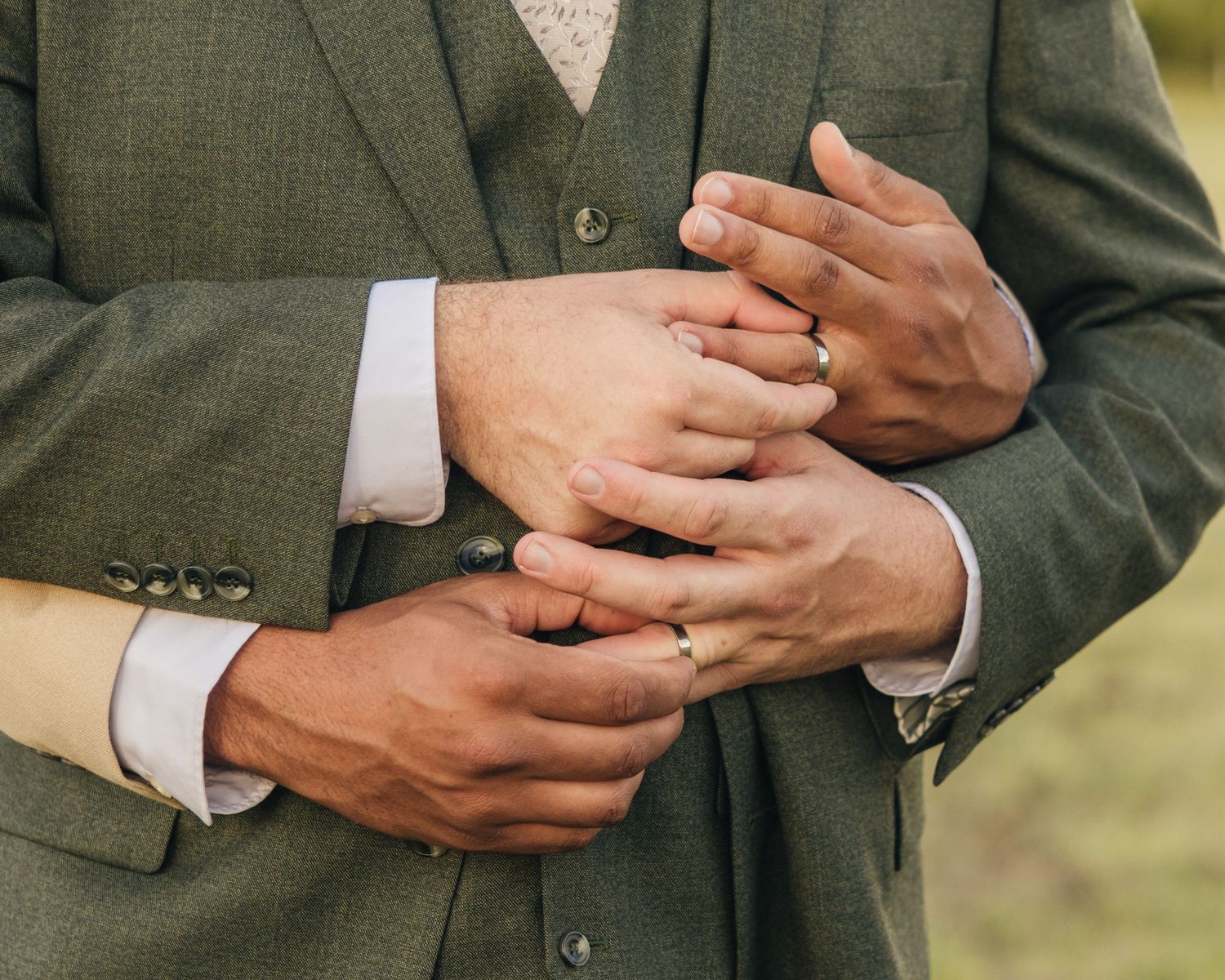 Close-up of Aaron and Jack’s hands showing their wedding rings against Jack’s green suit and white buttonhole.