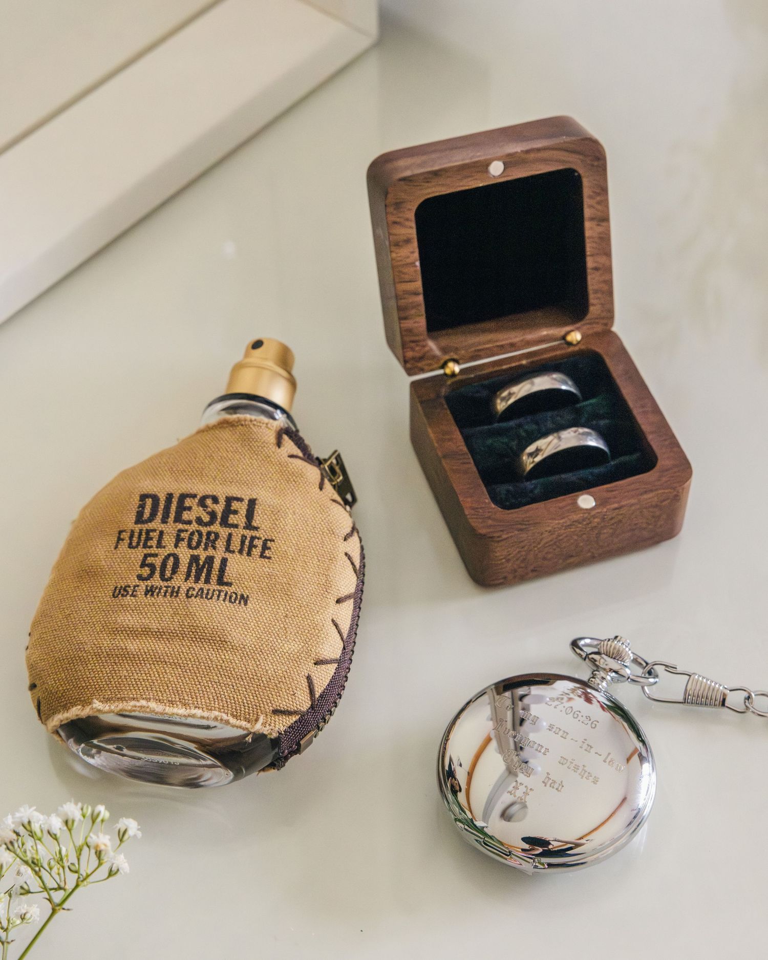 Aaron and Jack’s wedding rings displayed in a wooden box beside a pocket watch, some flowers and some perfume.