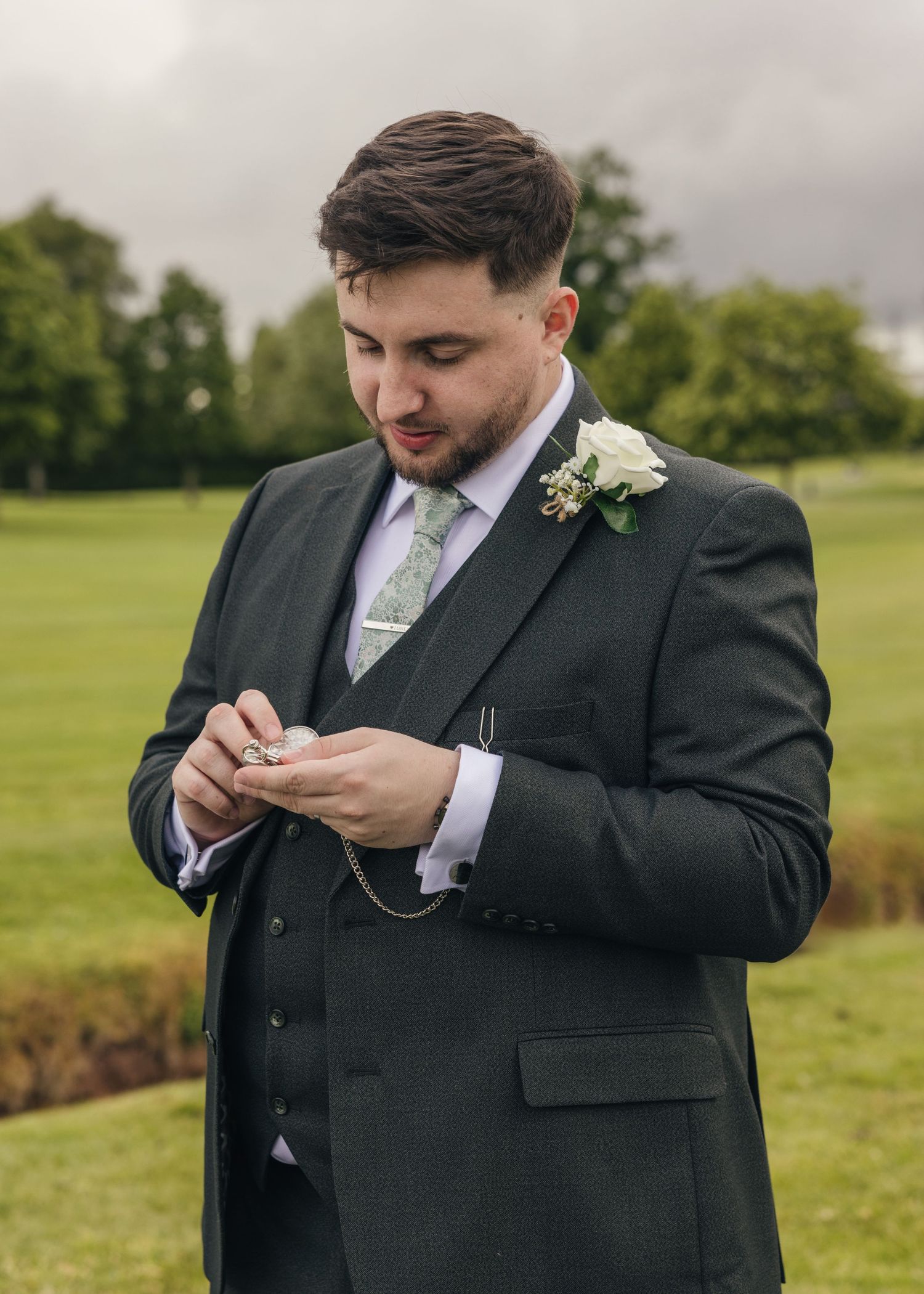 Dan checking his pocket watch while wearing his dark wedding suit and patterned tie.