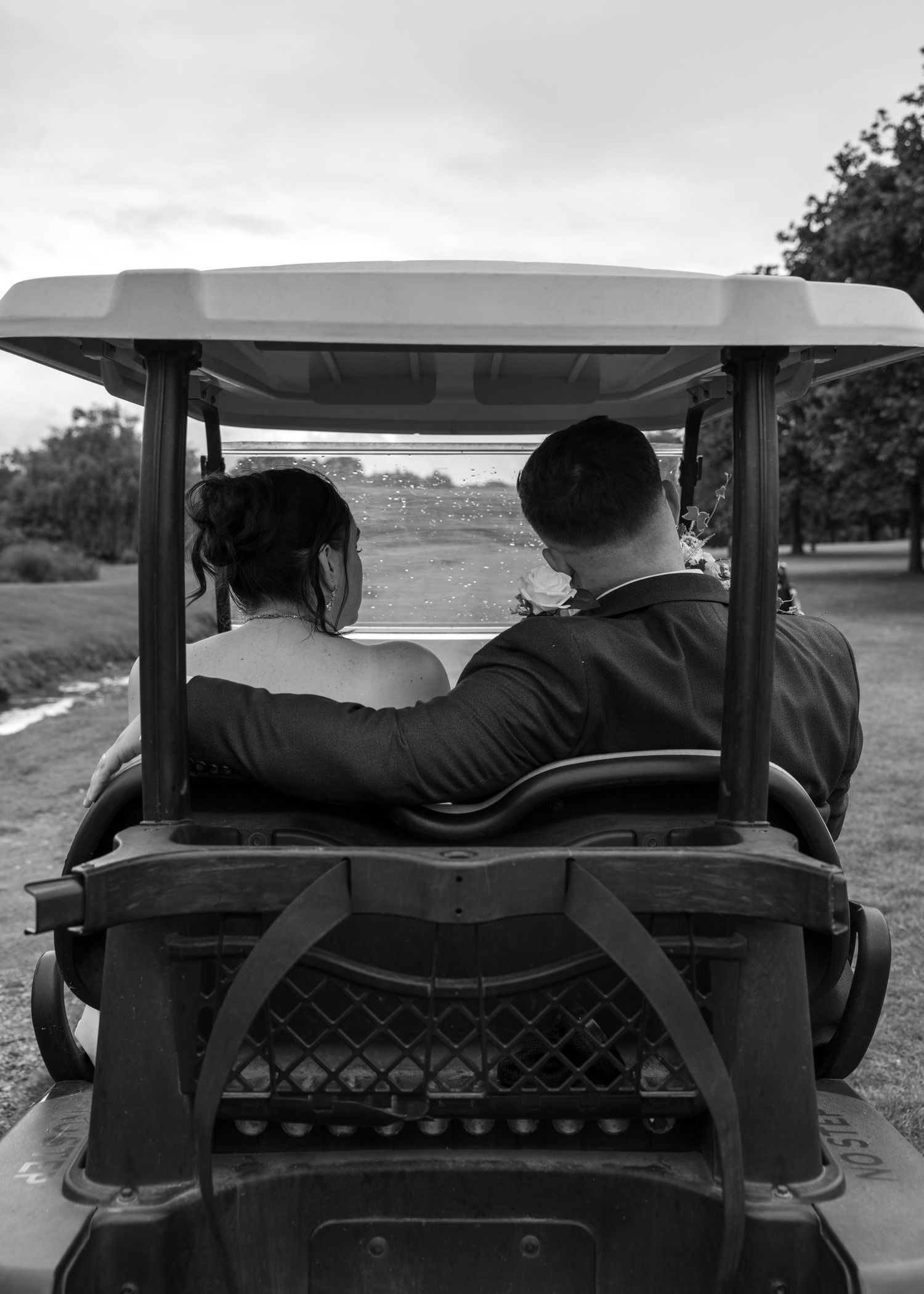 Black-and-white candid photograph of Cortney and Dan riding together in a golf cart across the grounds.