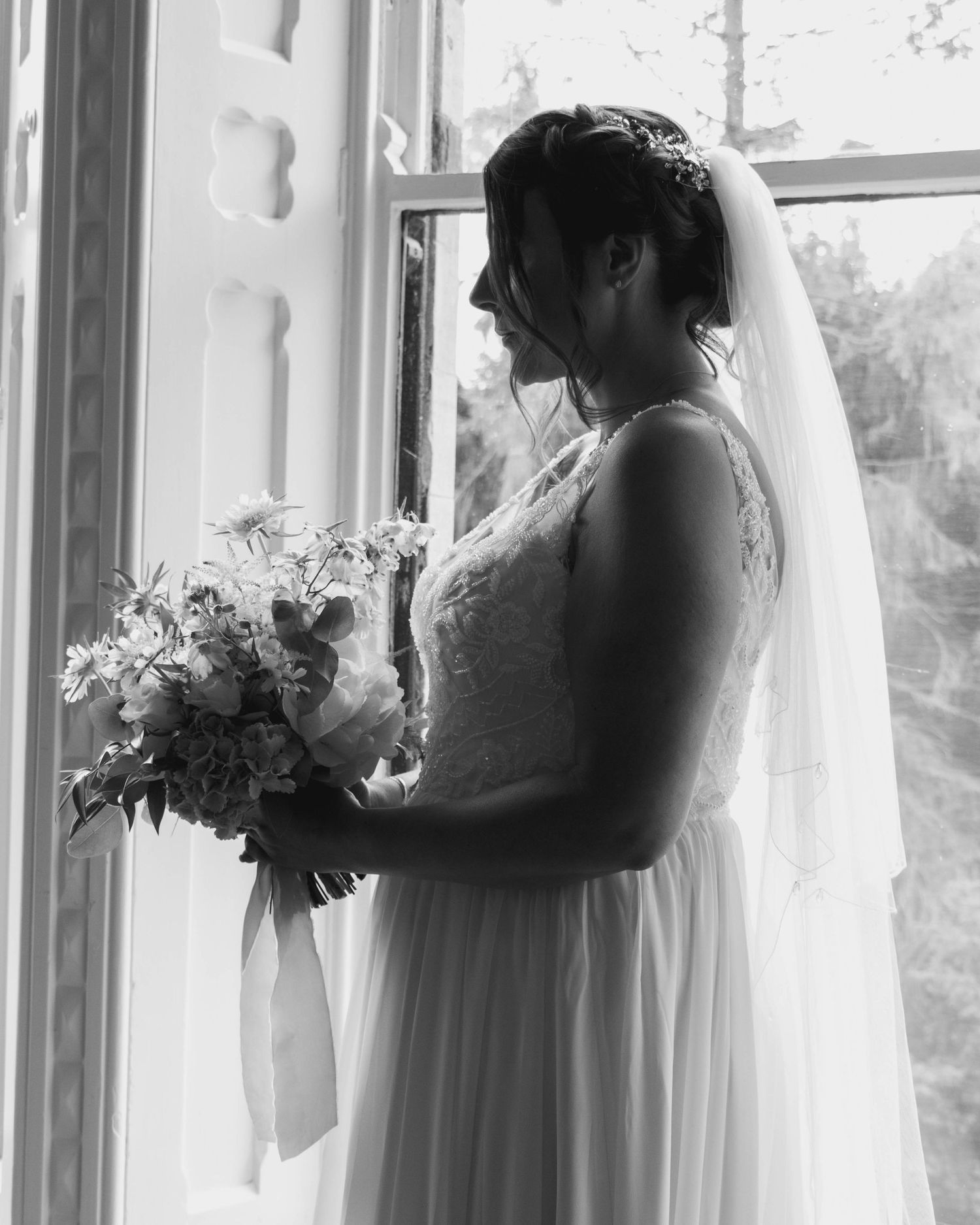 Bride taking a moment after bridal prep, in front of a window wearing a veil, captured by EvieSJPhotography.
