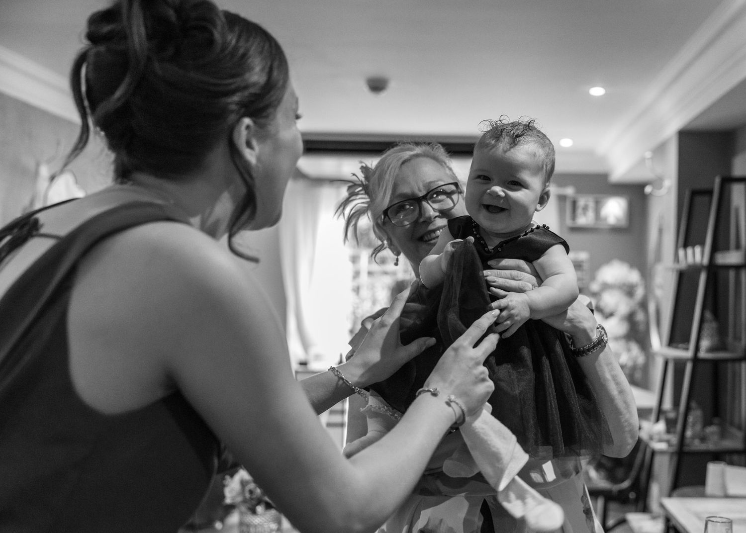 Grandmother holding a smiling baby while the child's mother shares the moment at the wedding reception.