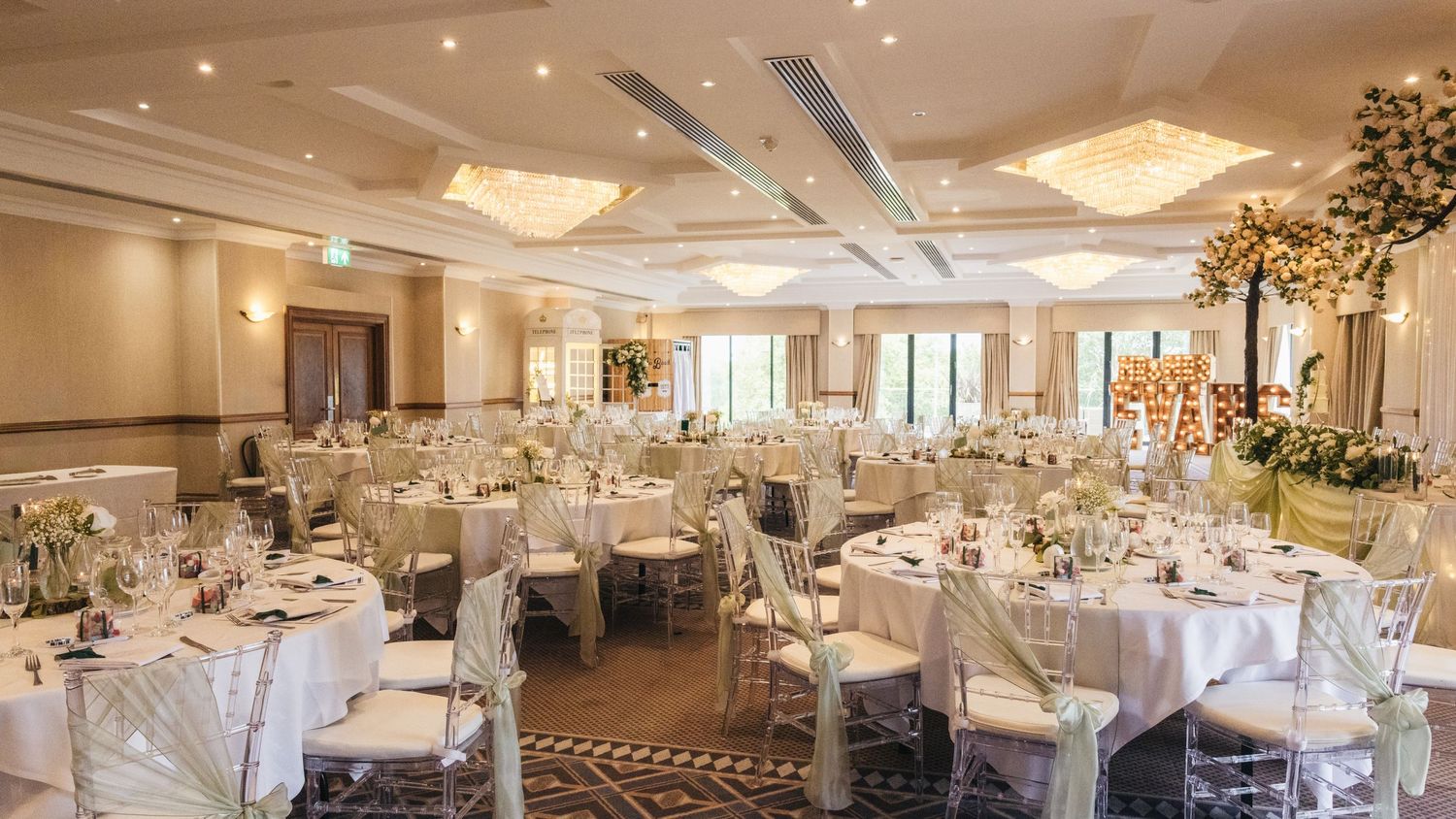 Wedding reception room at Windmill Village Hotel set with round tables, floral arrangements and chandeliers.