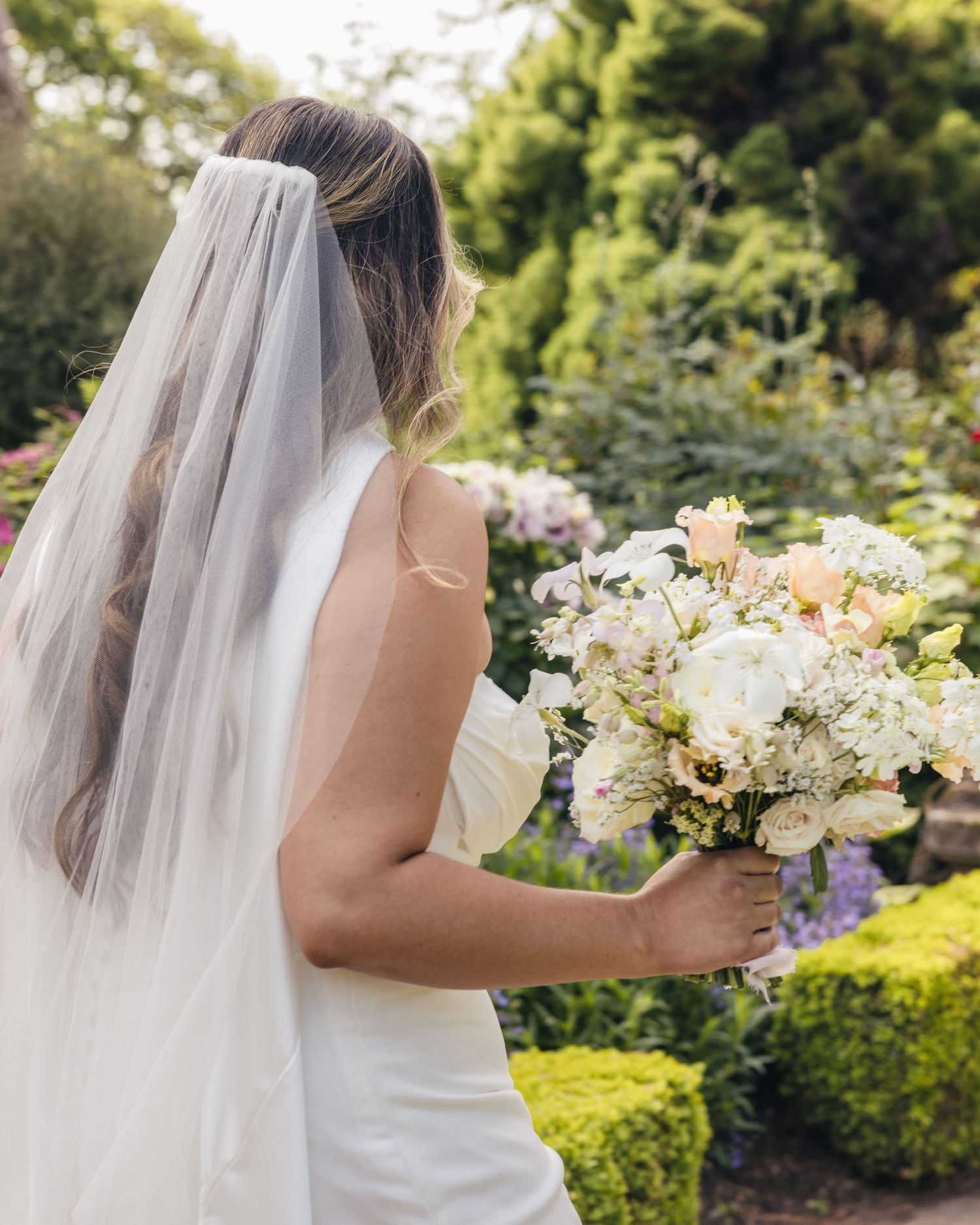 A bride holding her floral bouquet, walking to meet her future husband, captured by EvieSJPhotography.
