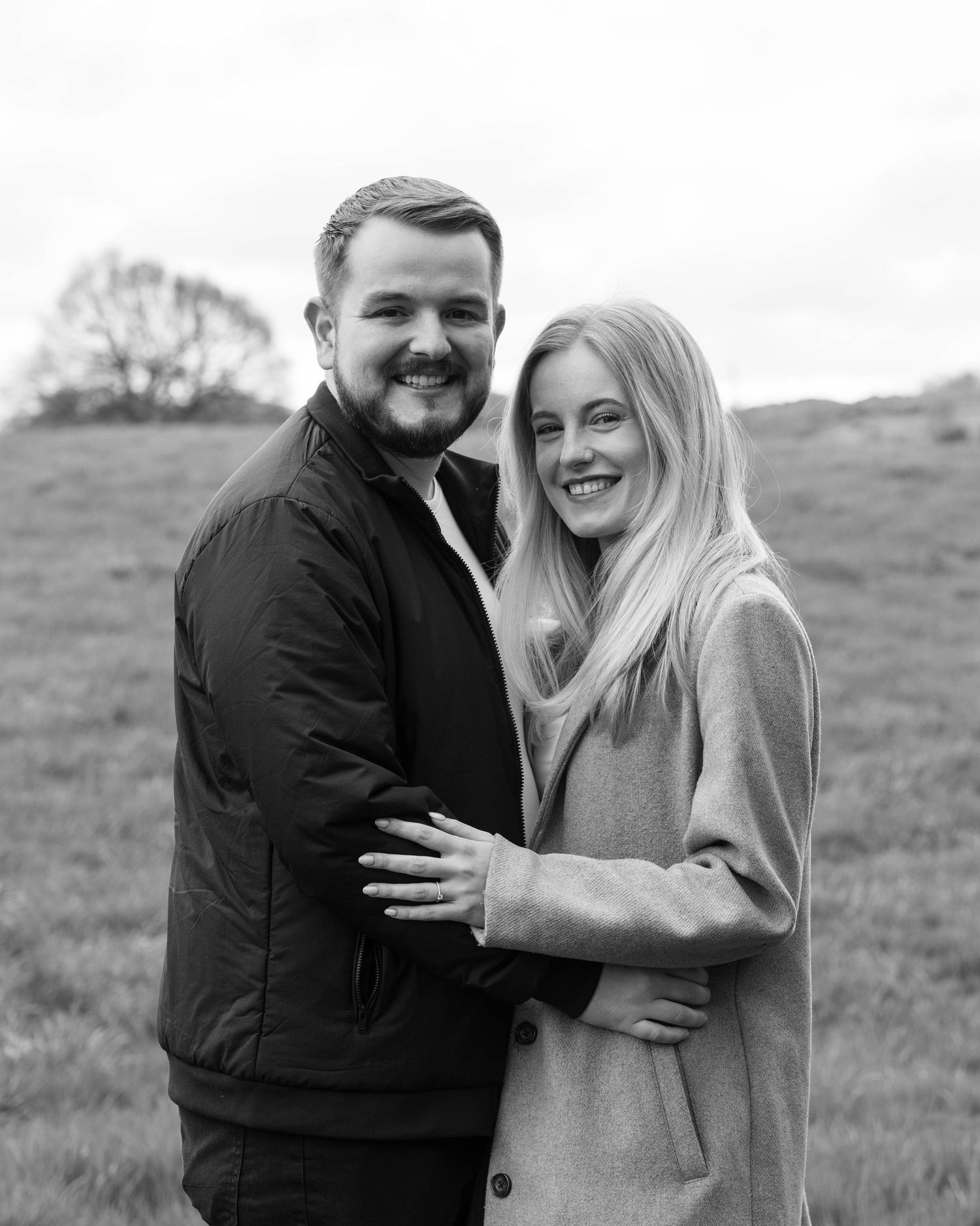 Natural black and white engagement photoshoot of a couple in a field by EvieSJPhotography.