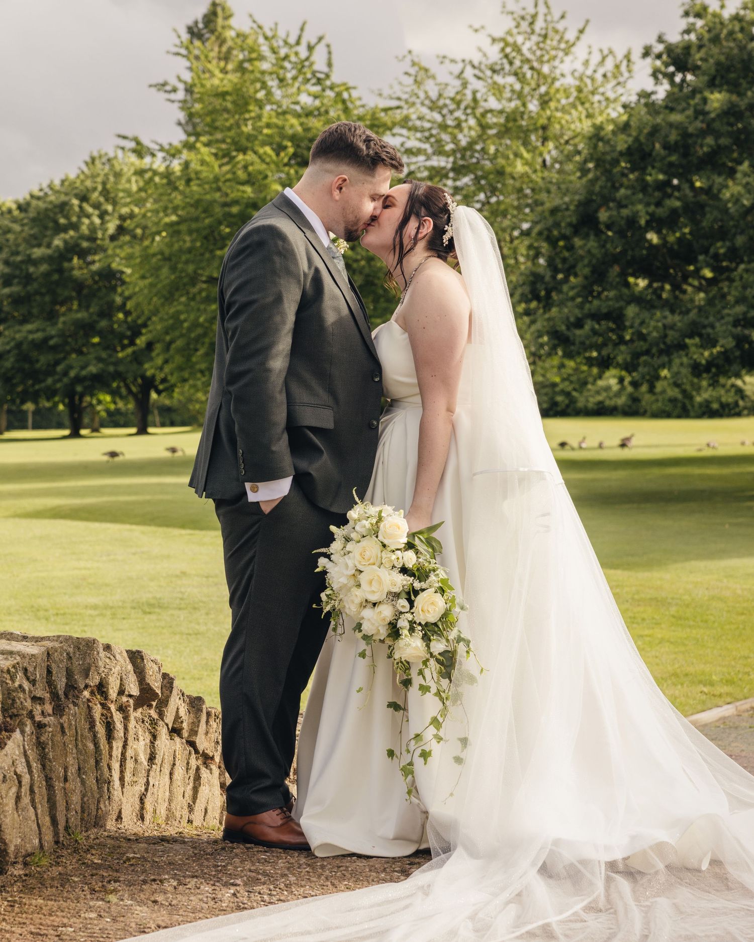 Cortney and Dan sharing a kiss beside a stone bridge on the hotel's landscaped golf course.