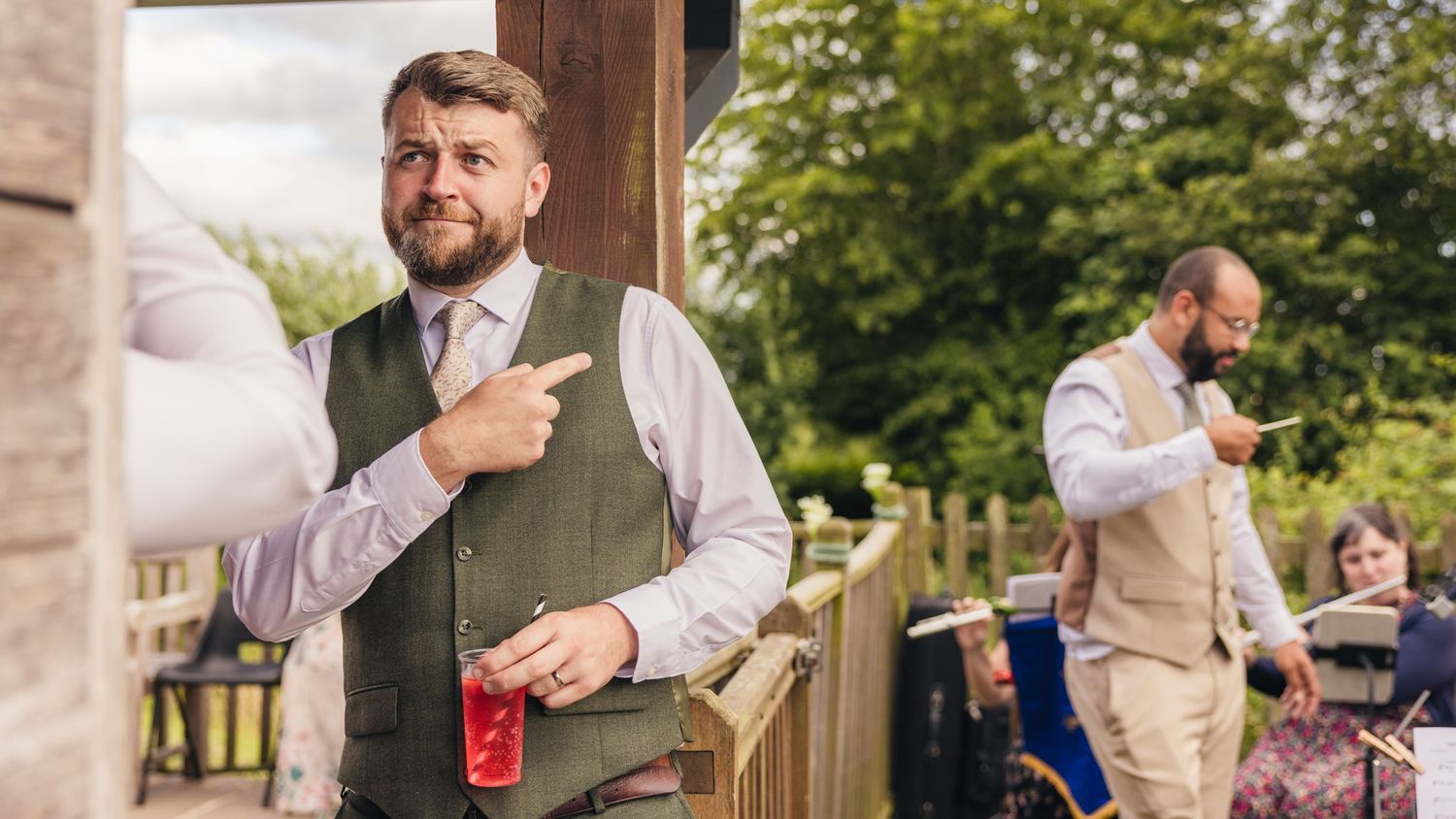 Jack holds a drink and gestures playfully while Aaron stands beside the live band during their wedding reception.
