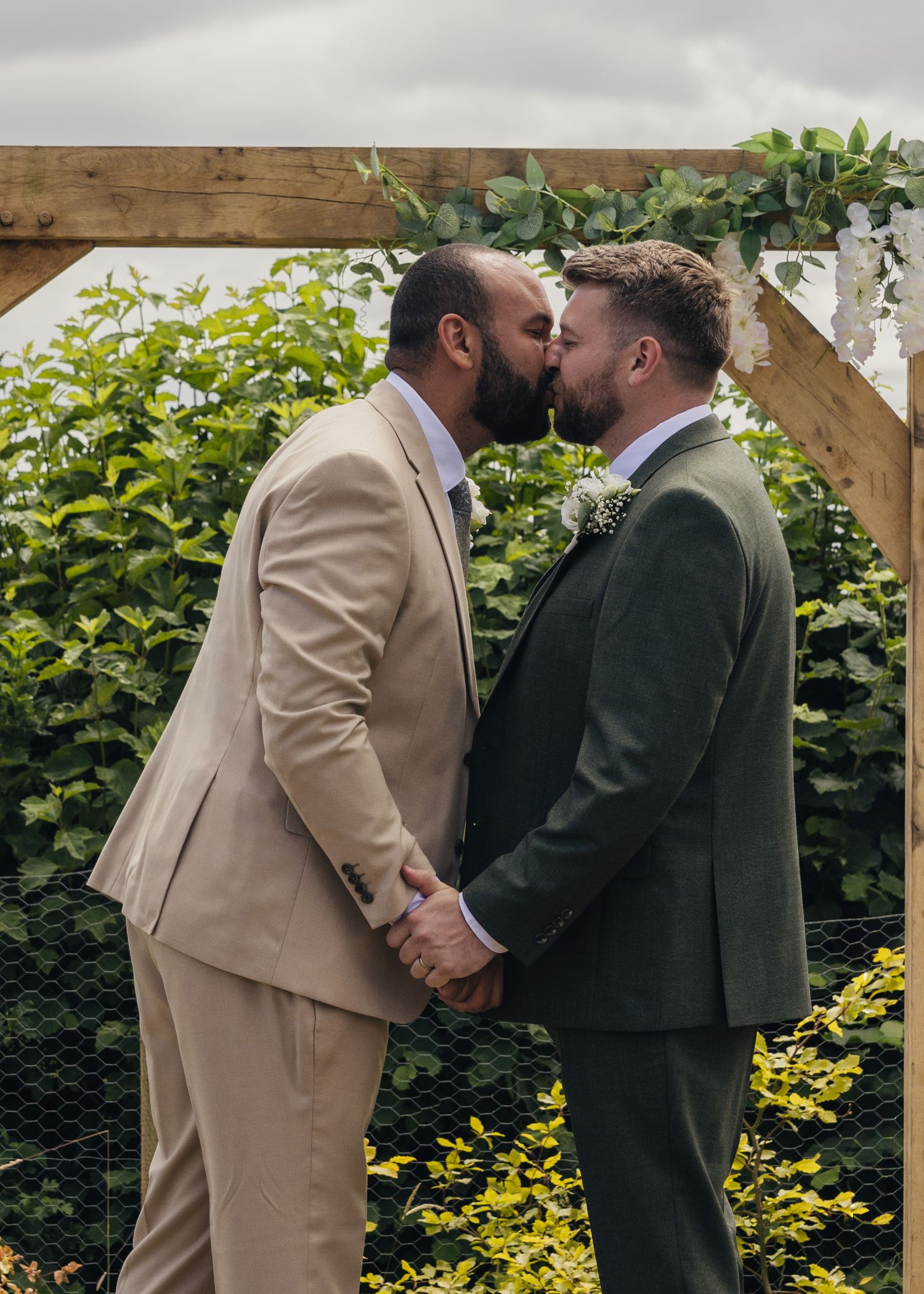 Aaron and Jack share their first kiss as a married couple beneath the flower-covered wooden arch during their outdoor ceremony.