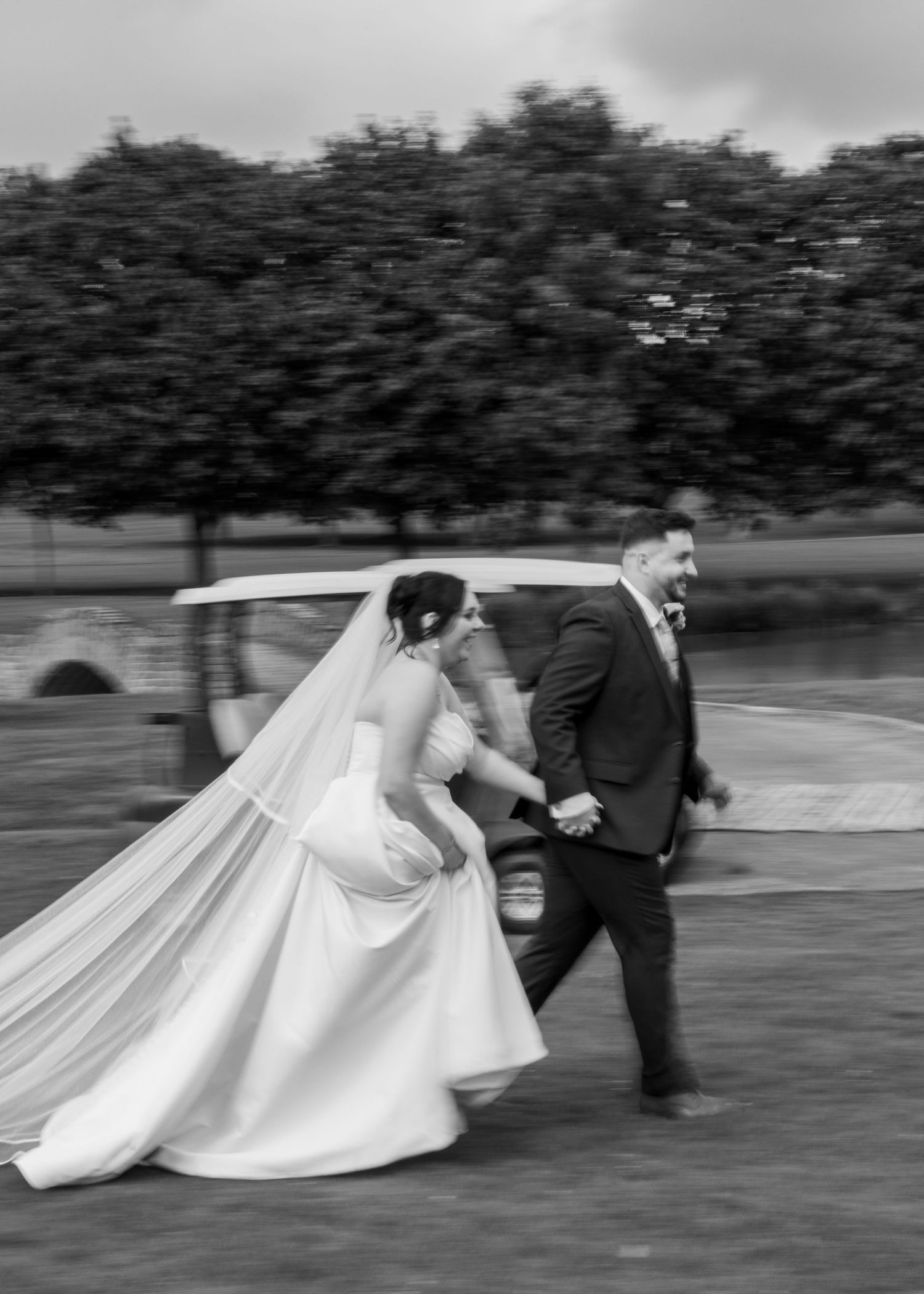 Cortney and Dan laughing as they run beside a golf cart in a playful black-and-white wedding photograph.