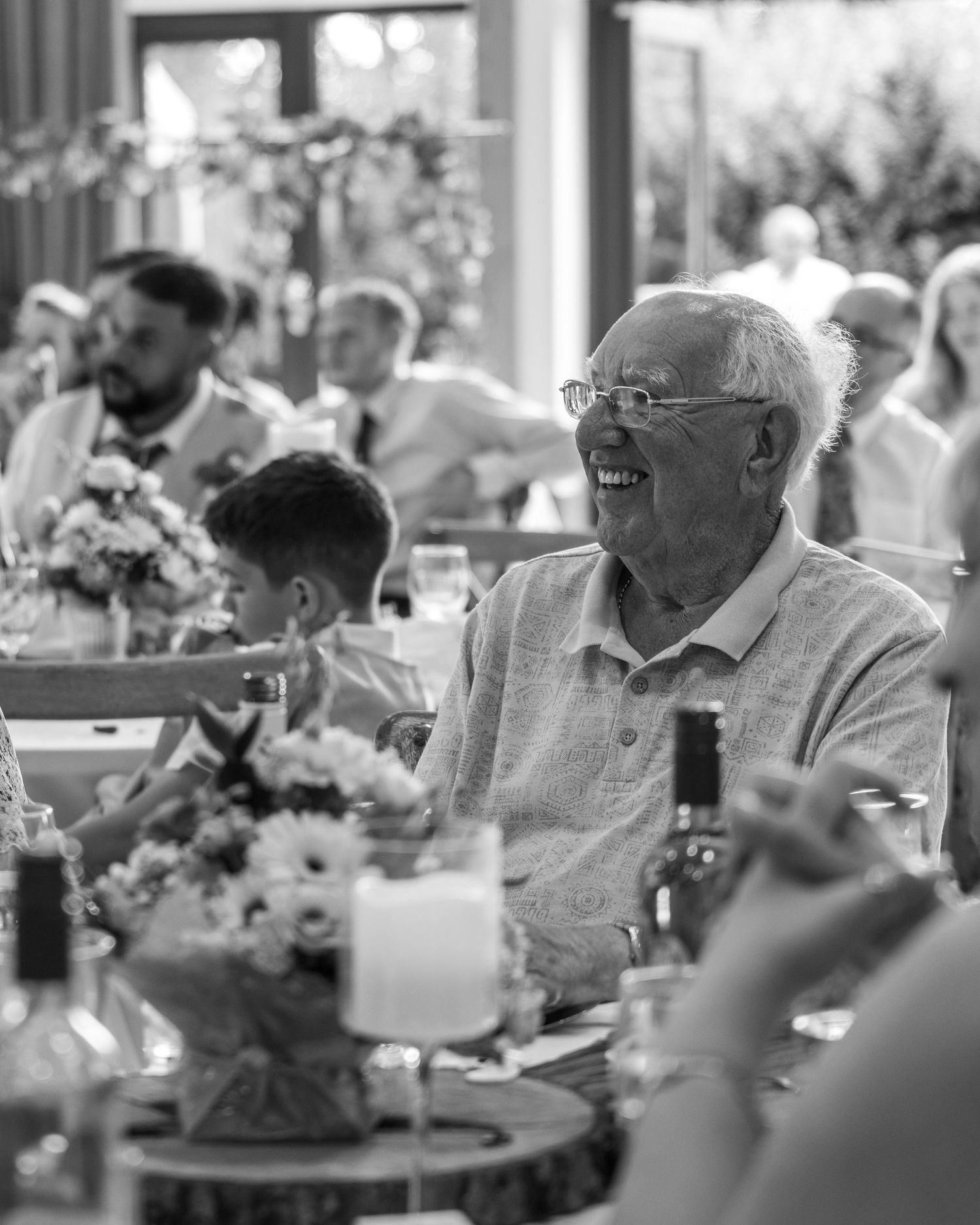An older gentleman smiling during the wedding speeches in an emotional black-and-white photograph.