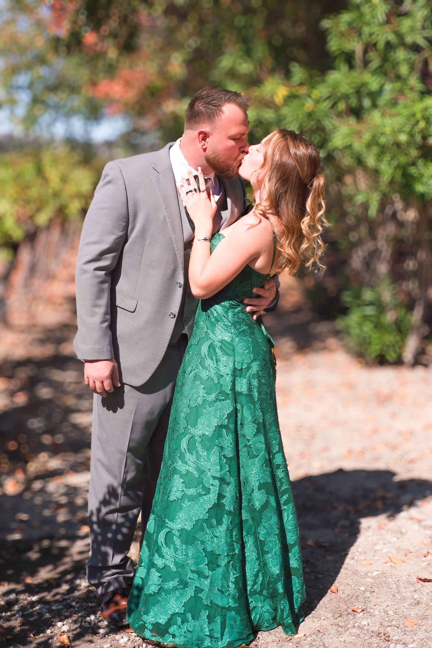 Couple in formal attire sharing intimate moments against a natural autumn backdrop.