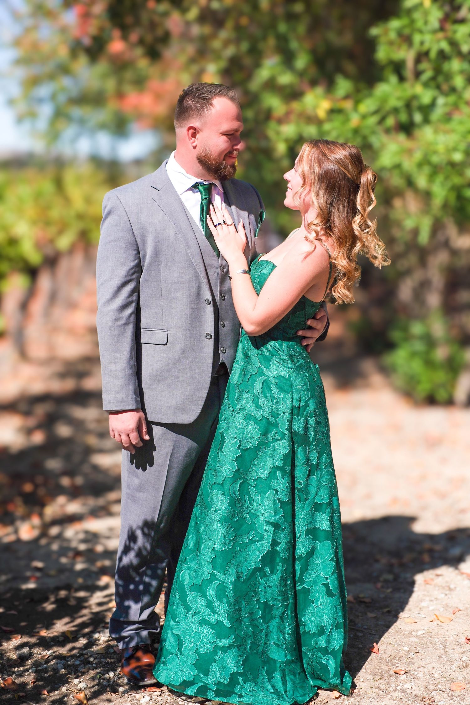 A couple in a grey suit and emerald green lace dress share intimate moments during an outdoor photo session.