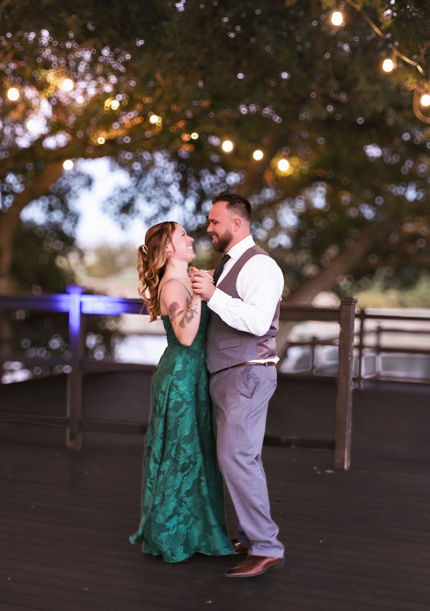A couple shares a romantic dance under twinkling lights at an outdoor evening reception.