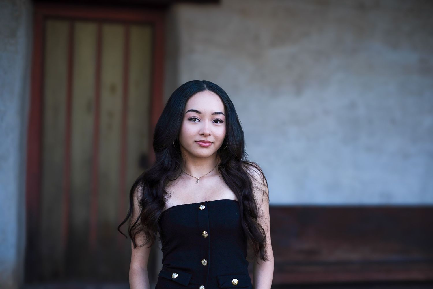 A woman with long dark hair poses against a gray background in a black sleeveless top.