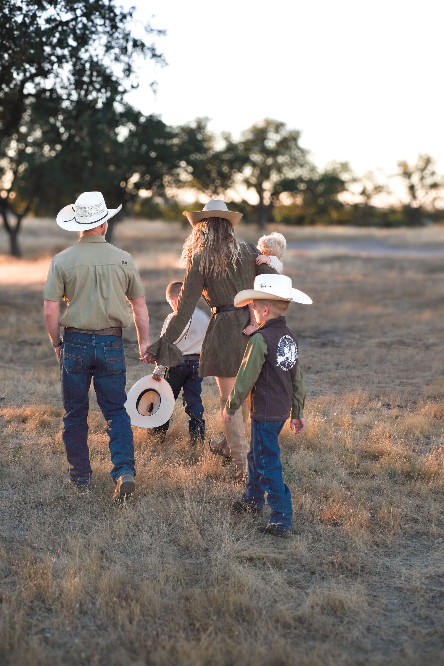 A family in cowboy hats walks together through a golden field during sunset, creating long shadows.