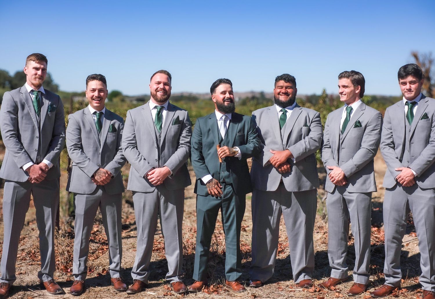 Groomsmen in matching gray suits sitting in a row on outdoor steps for a wedding photo.