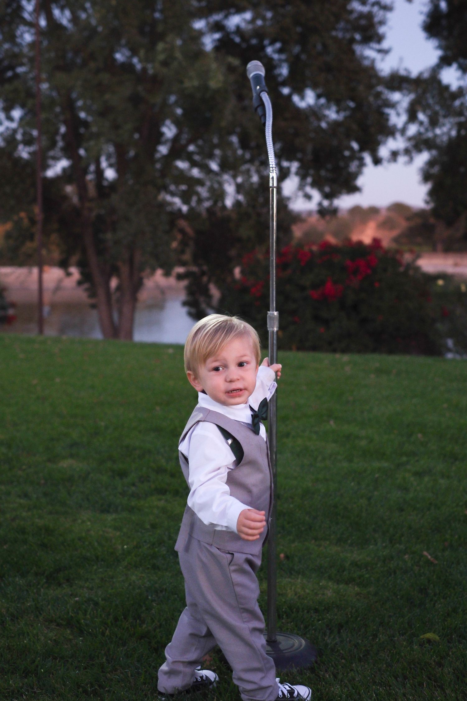 A small child in formal attire holds a golf club on a grassy lawn at sunset.