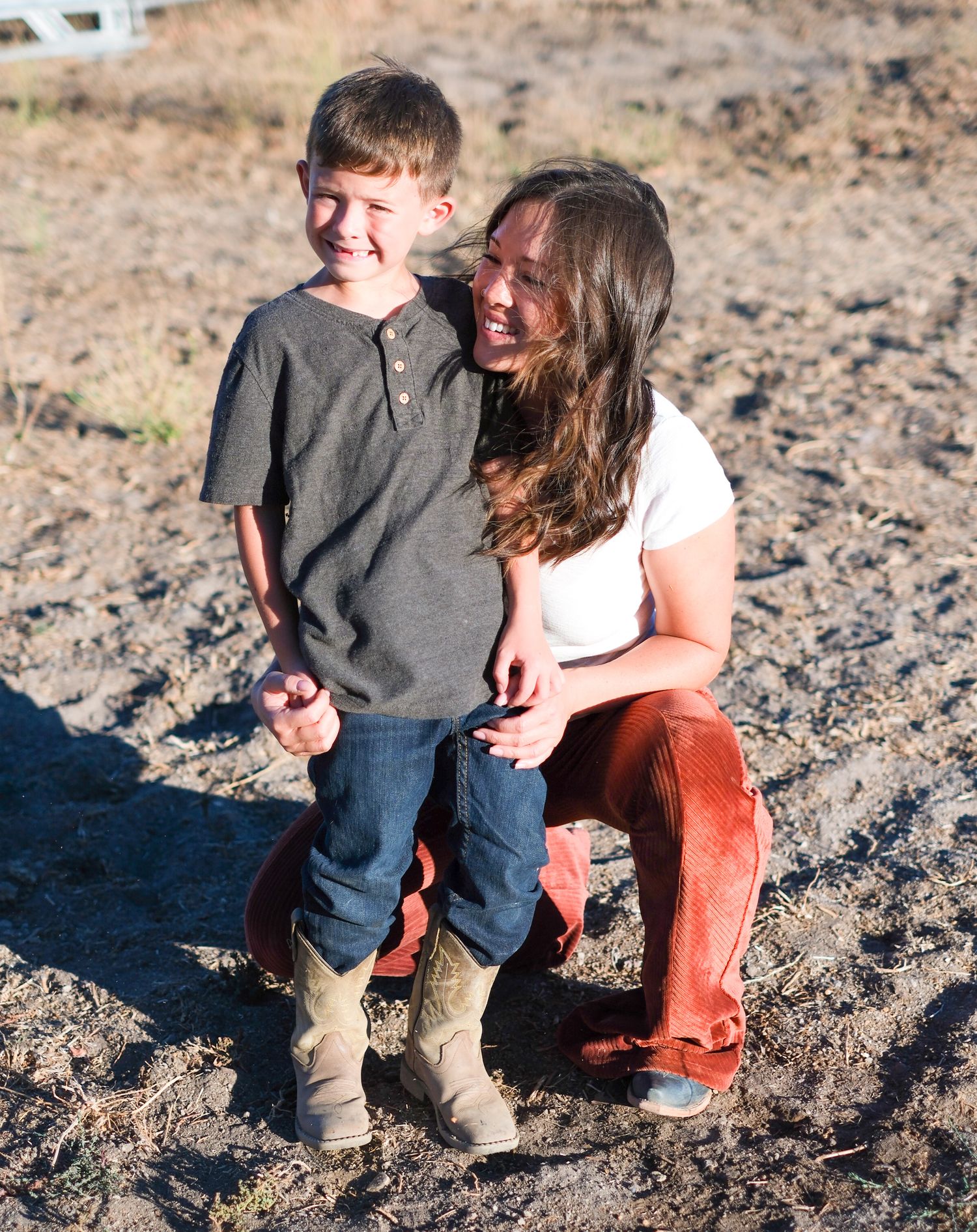 Parent and child sitting together on sandy ground during a casual outdoor photo session.