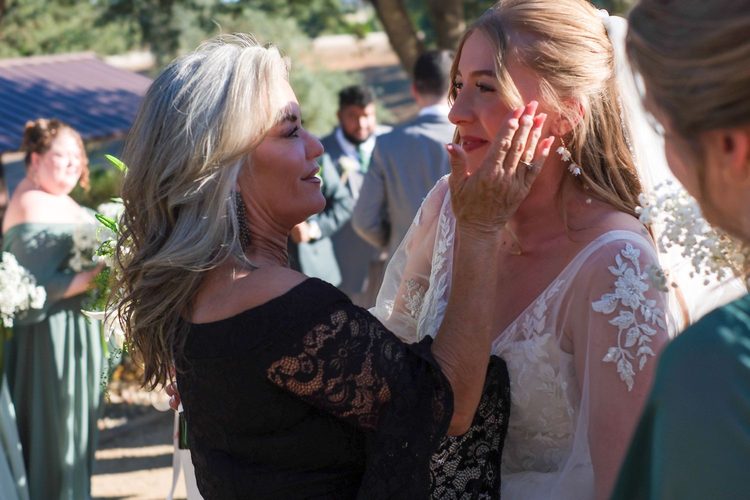 Two people share an emotional moment at an outdoor wedding celebration, one wearing black lace and one in white lace.
