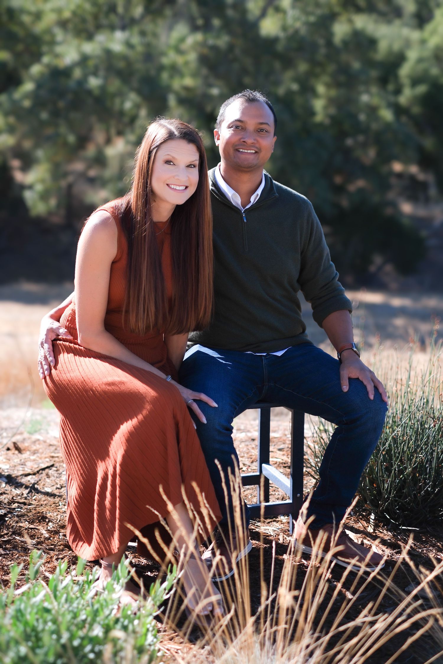 Couple sitting together in a grassy field during a sunny outdoor photoshoot.