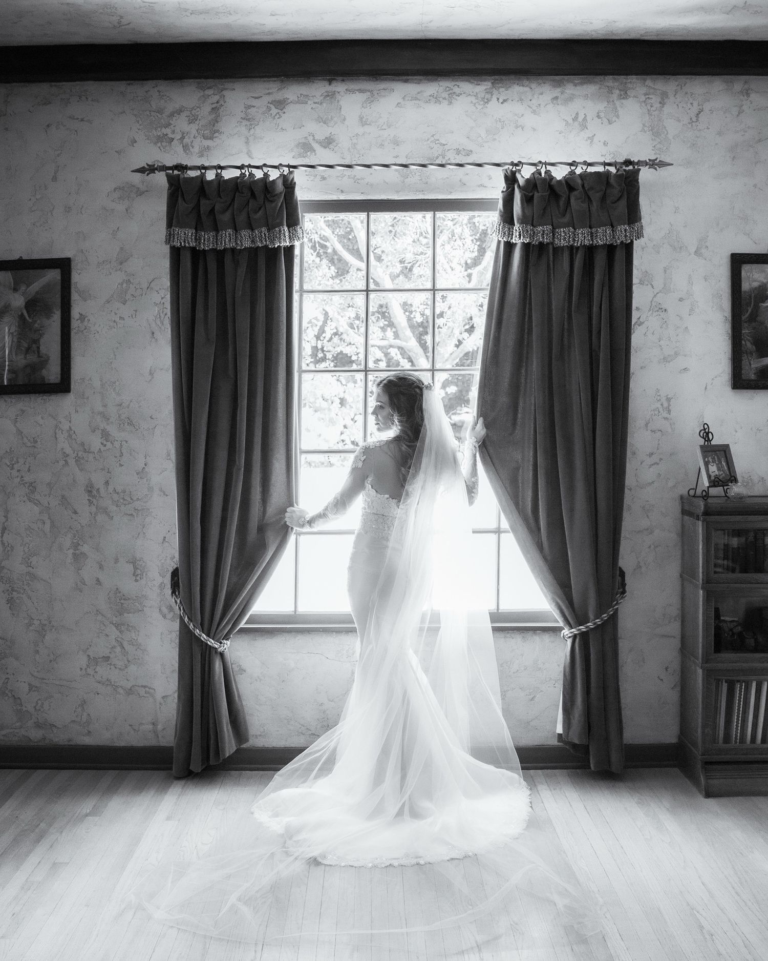 A flowing white wedding dress twirls gracefully in a sunlit room with dark curtains and hardwood floors.