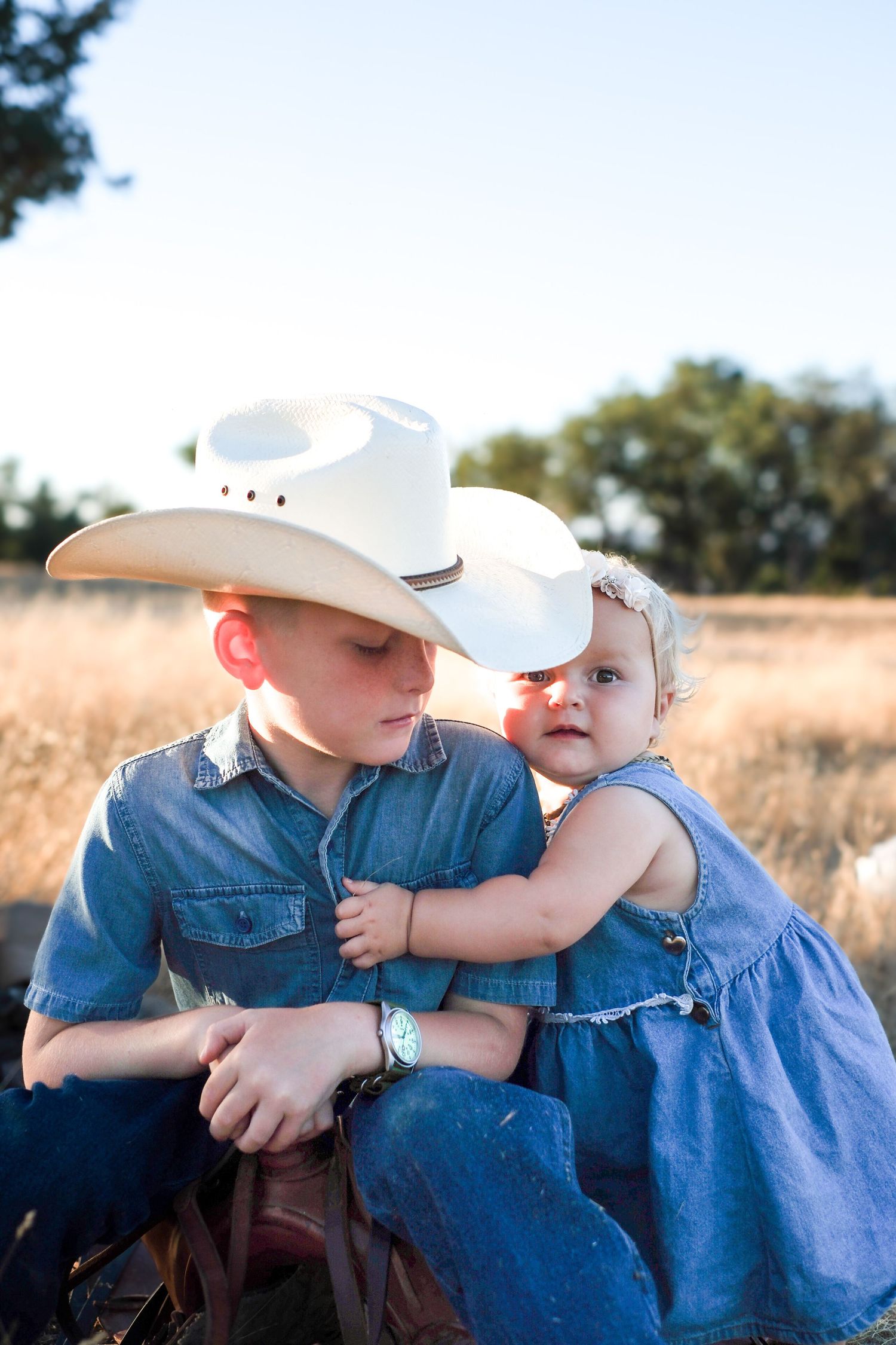 Two young cowboys in denim share a tender moment in a sunlit field.