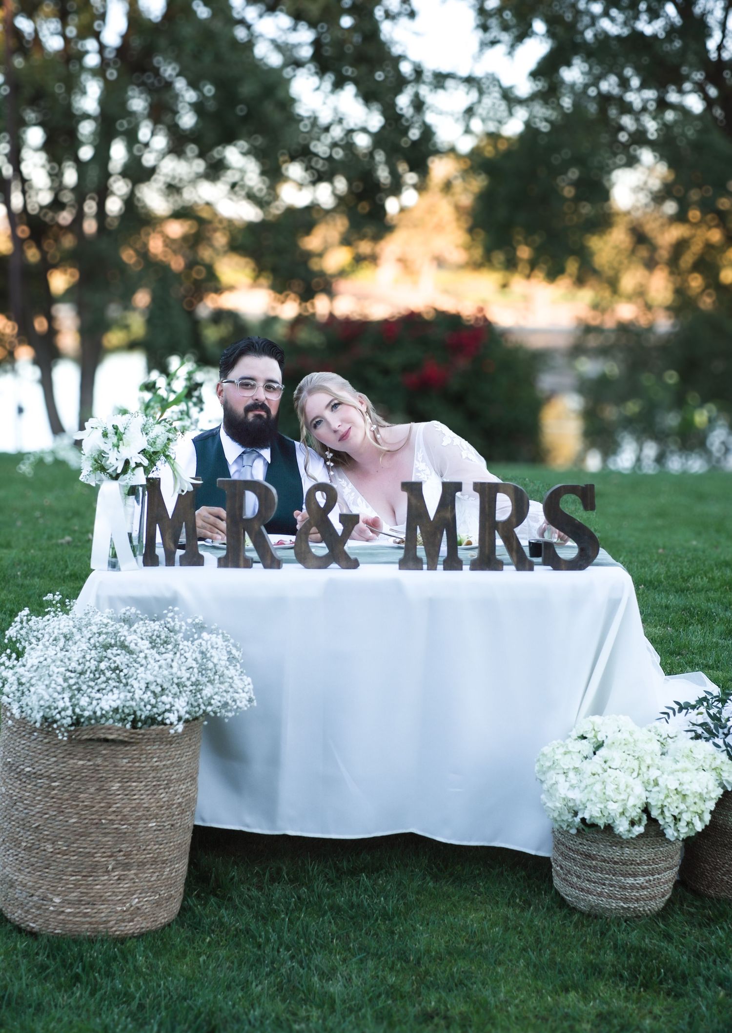 Rustic wedding decor featuring 'MR & MRS' sign with white baby's breath flowers in woven baskets on grass.
