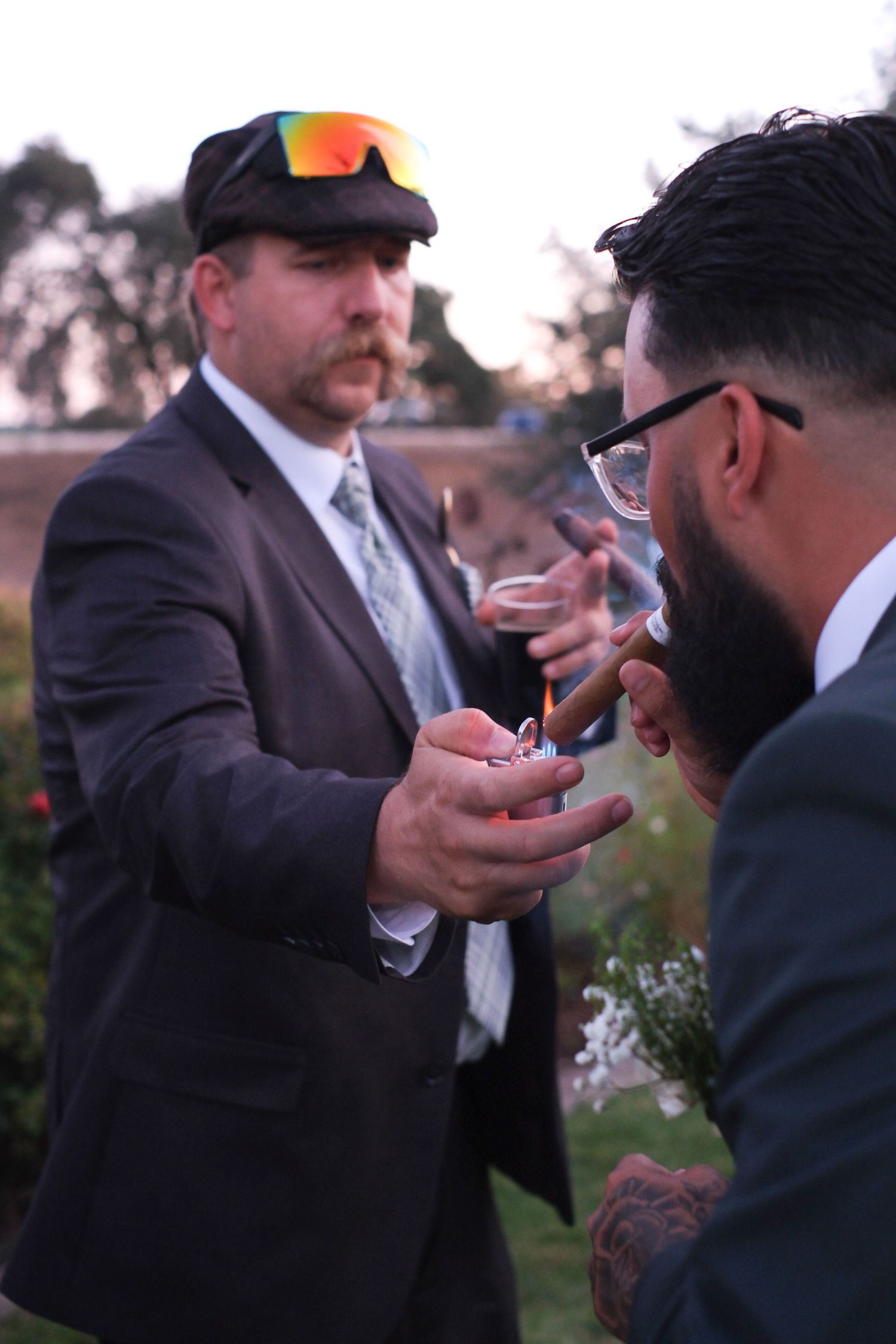Two men in suits share a playful moment during a wedding reception outdoors.