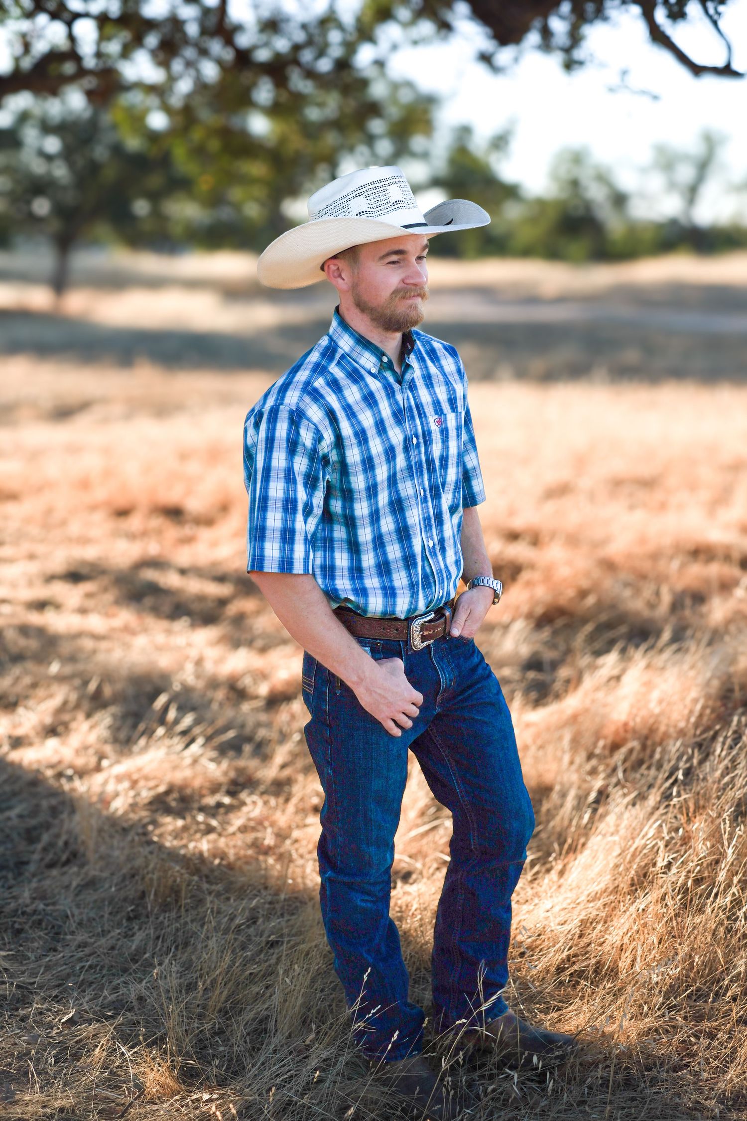Young boy in blue plaid shirt and jeans exploring a sun-lit grassy field during golden hour.