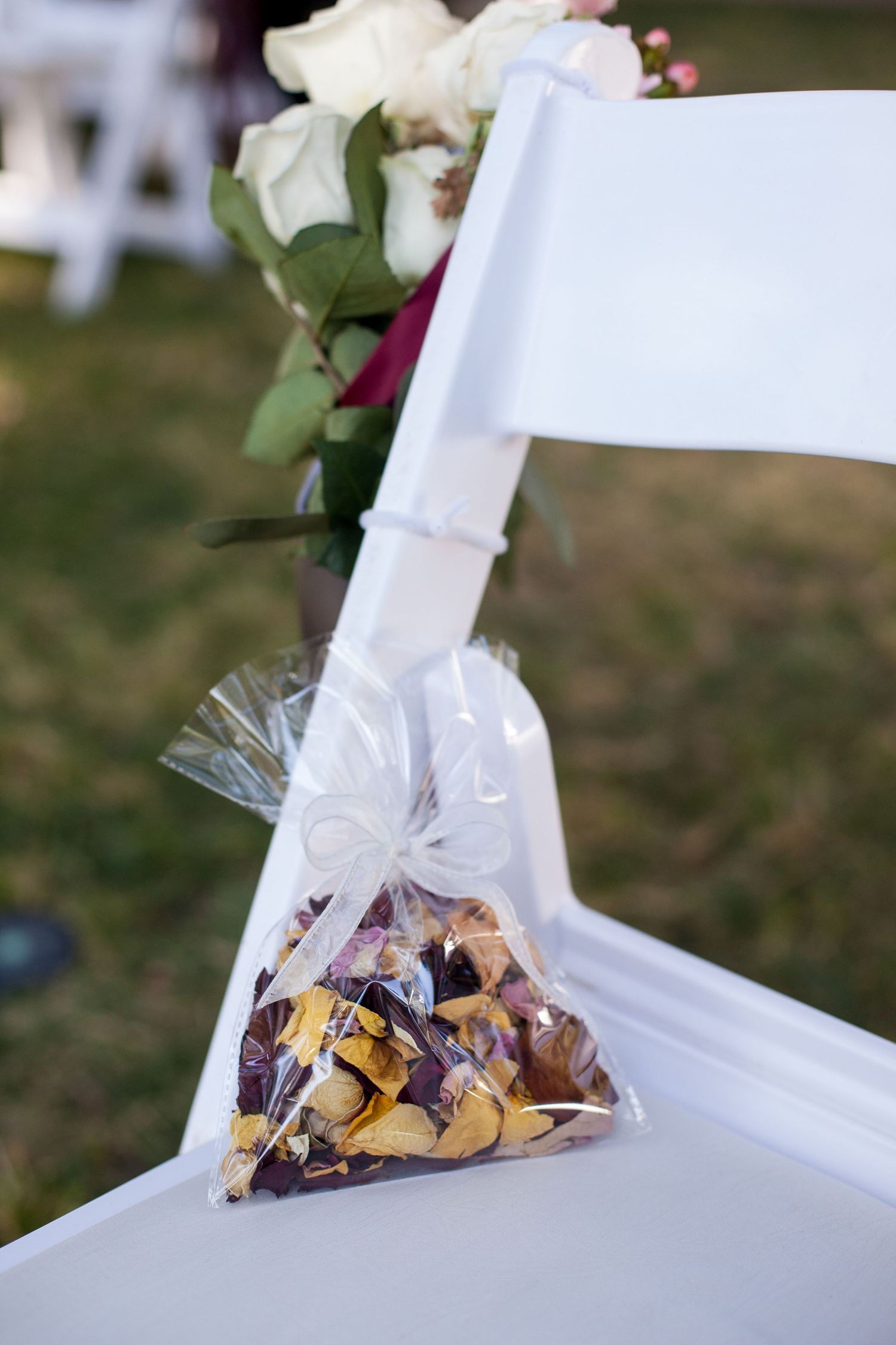 Small clear plastic bags filled with snacks or treats are tied with white ribbons to white wooden chairs outdoors.
