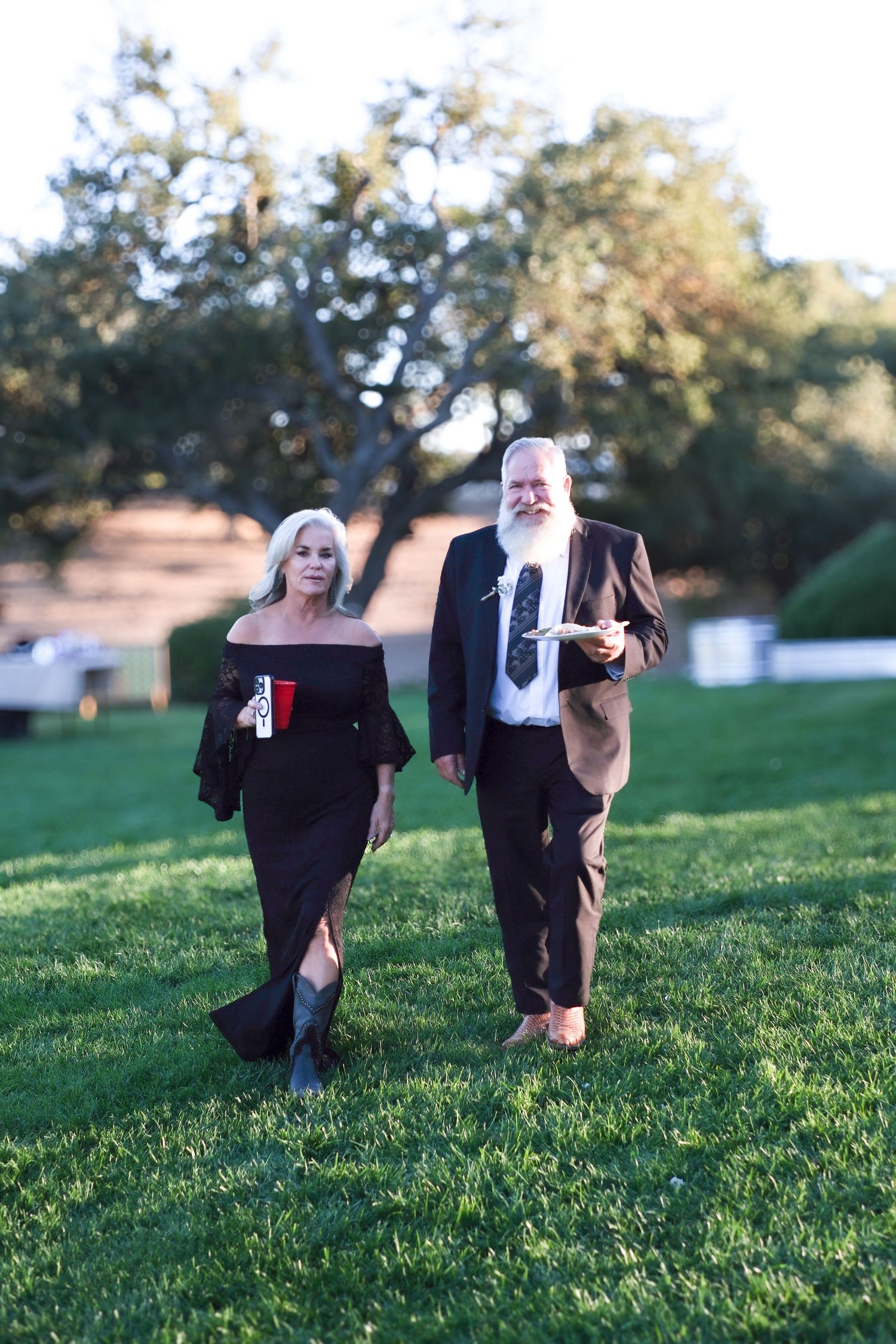 Wedding party members in formal attire running and posing playfully on a grassy hill.