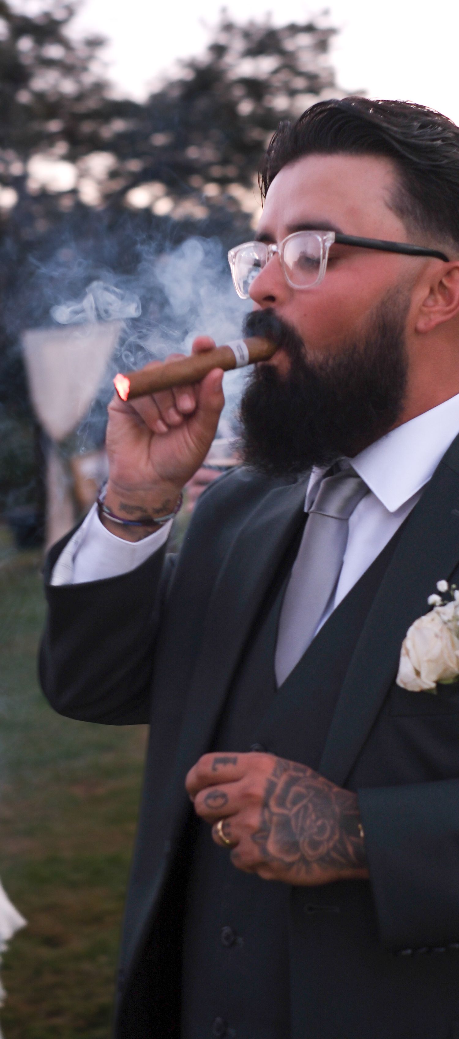 Series of shots showing a bearded man in a suit smoking a cigar at dusk.