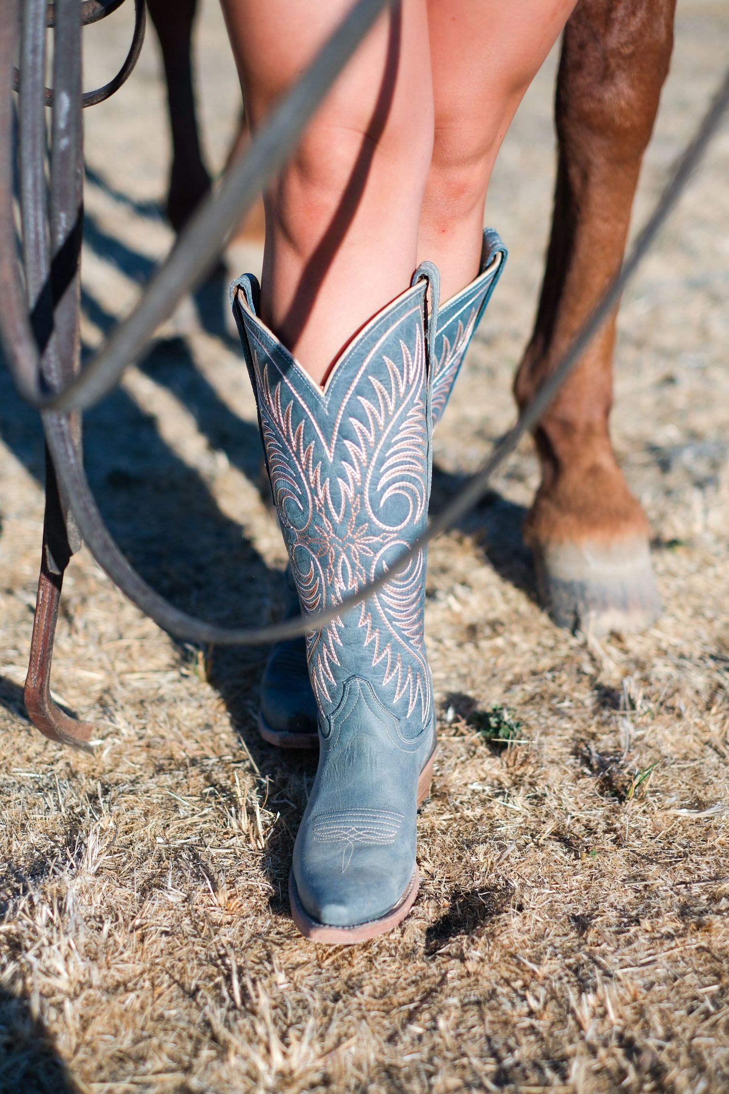 Close-up of blue and white decorative cowboy boots against dusty ground.