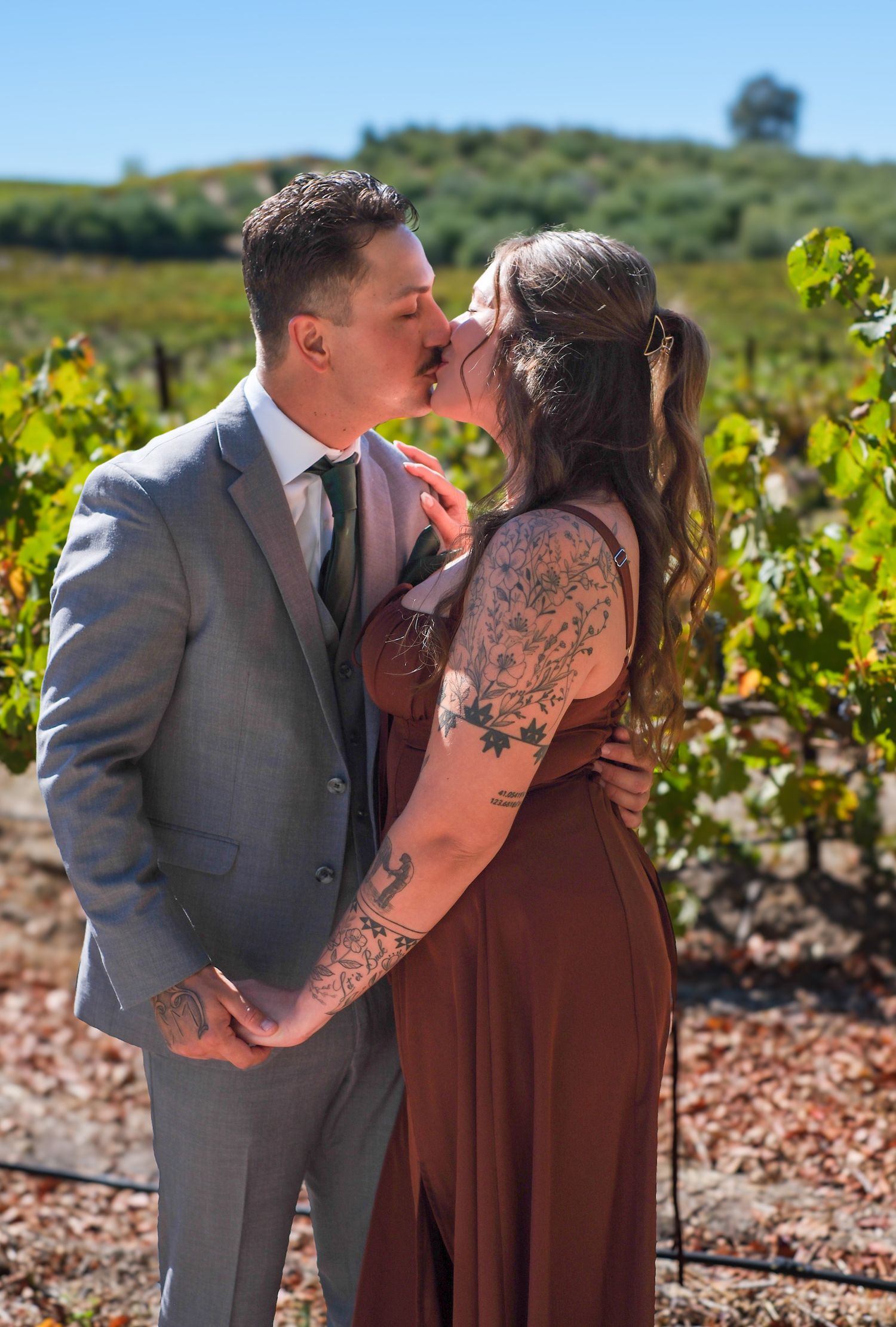 A couple shares an intimate moment among vineyard rows on a sunny day.