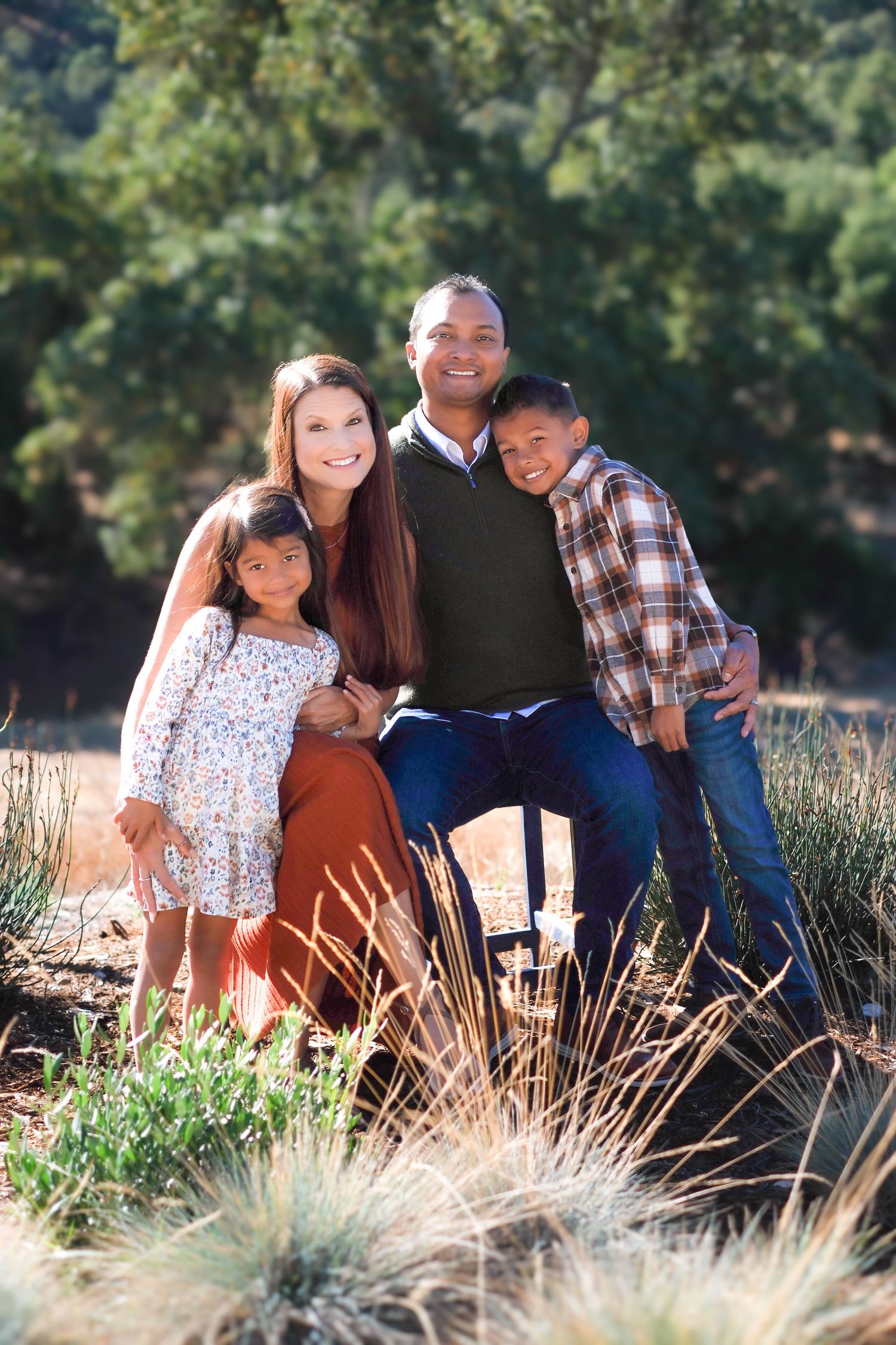 Family enjoying a casual outdoor photo session in tall grass and sunlight.