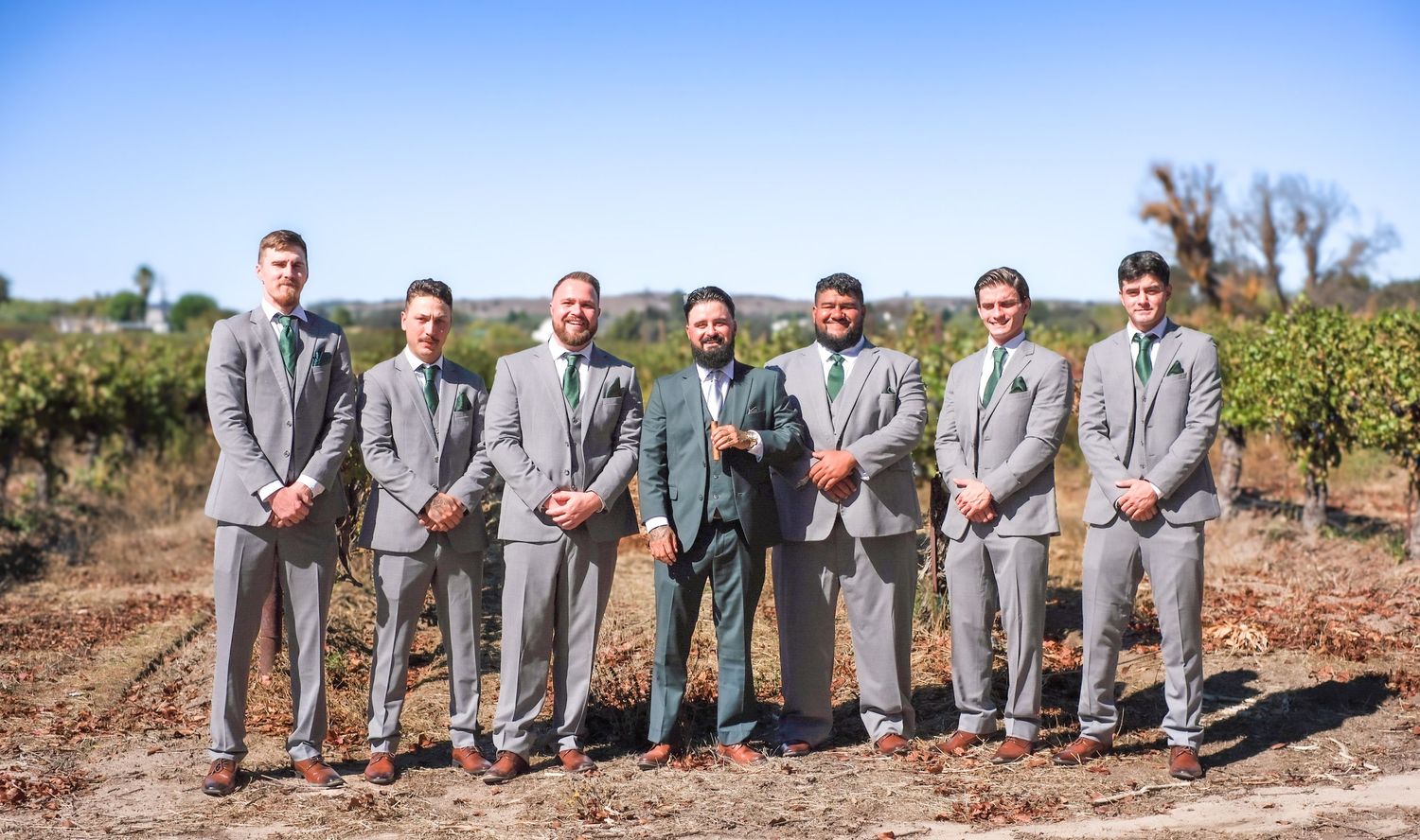Groomsmen in matching grey suits show off their colorful socks while sitting on a stone wall.