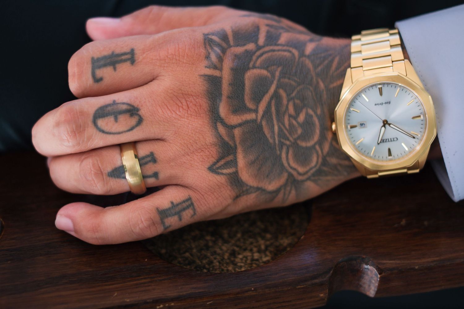 Close-up shots of tattooed hands wearing a gold watch against a dark wooden surface.