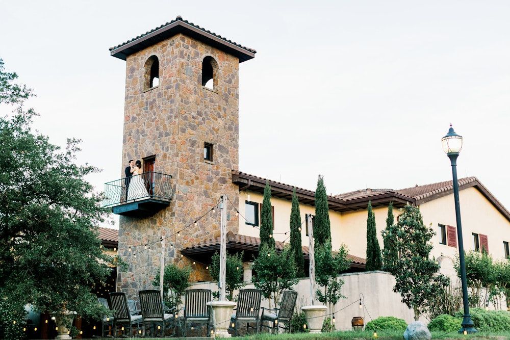 Mediterranean style church tower with bell and terracotta roof tiles against a bright blue sky.