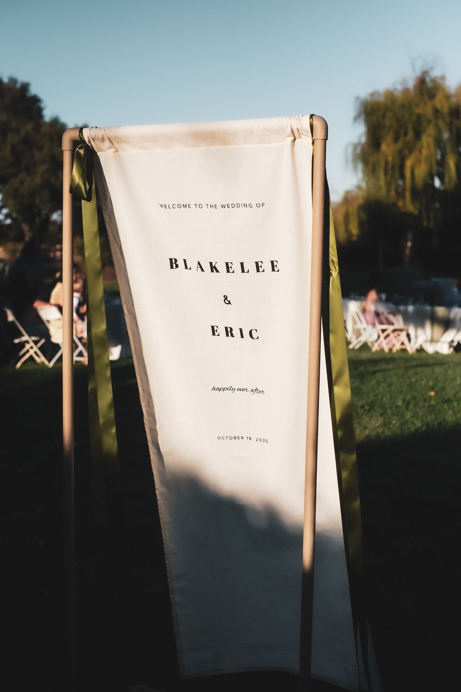 Wedding ceremony signage displays names 'Blakelee' and 'Eric' on white banners against a natural outdoor setting.