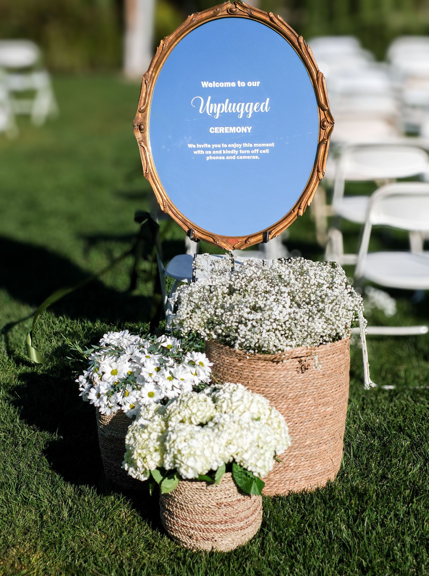 Rustic burlap-wrapped flower arrangements with white baby's breath flowers sit on grass as outdoor wedding decor.
