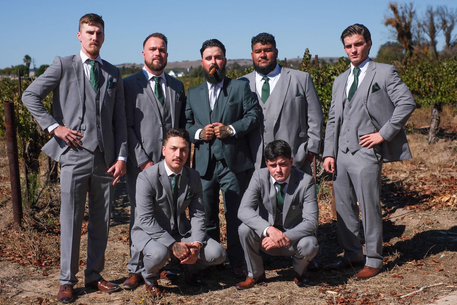 Wedding party in gray suits poses playfully on rocks during outdoor photo session at scenic desert location.