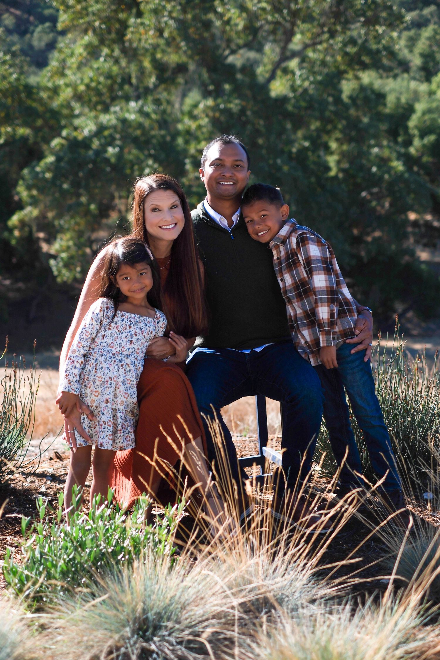 A family sits together outdoors in a natural setting with tall grass and sunlight creating a warm atmosphere.