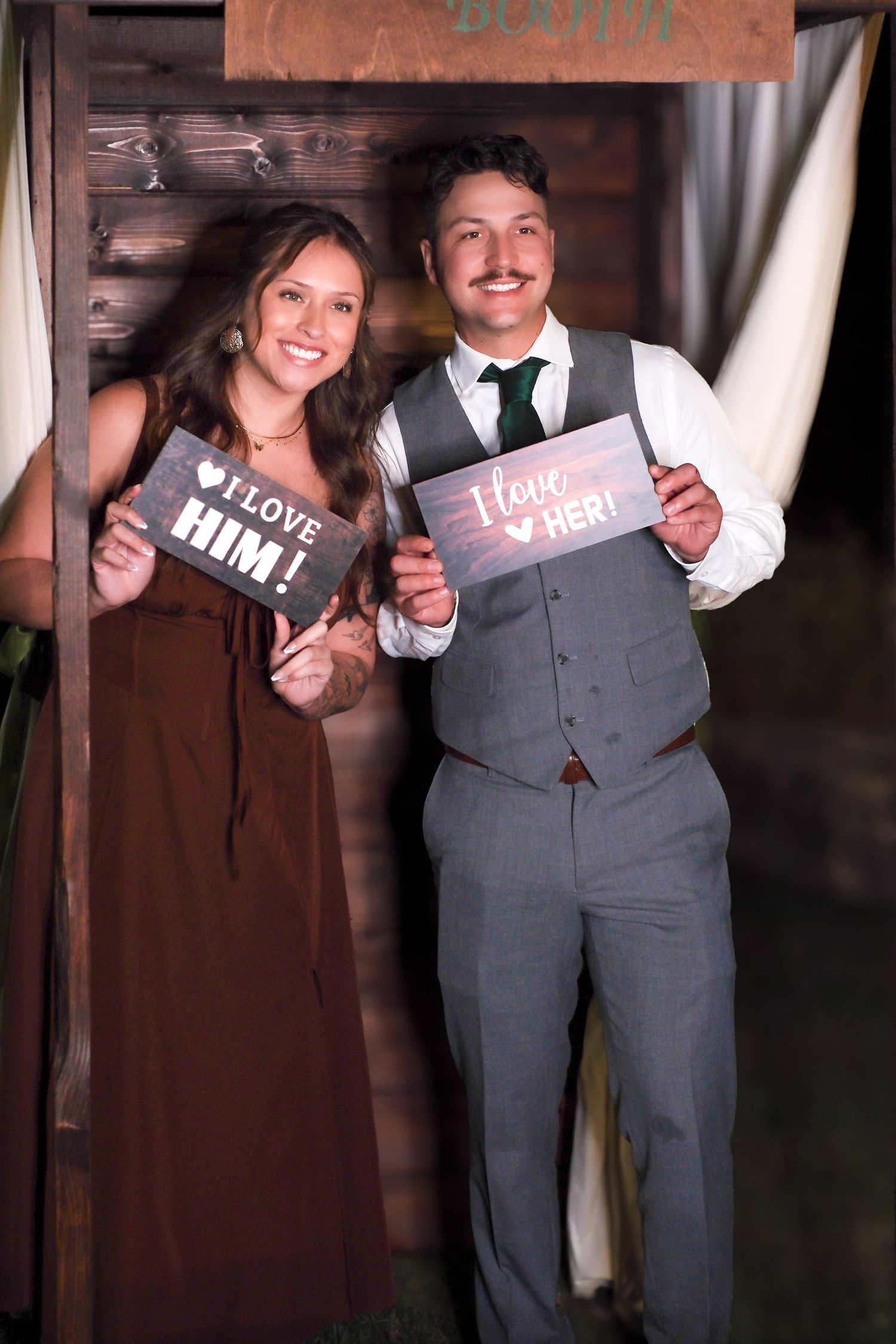 Wedding couple holds up decorative signs in a rustic barn setting with wooden walls.