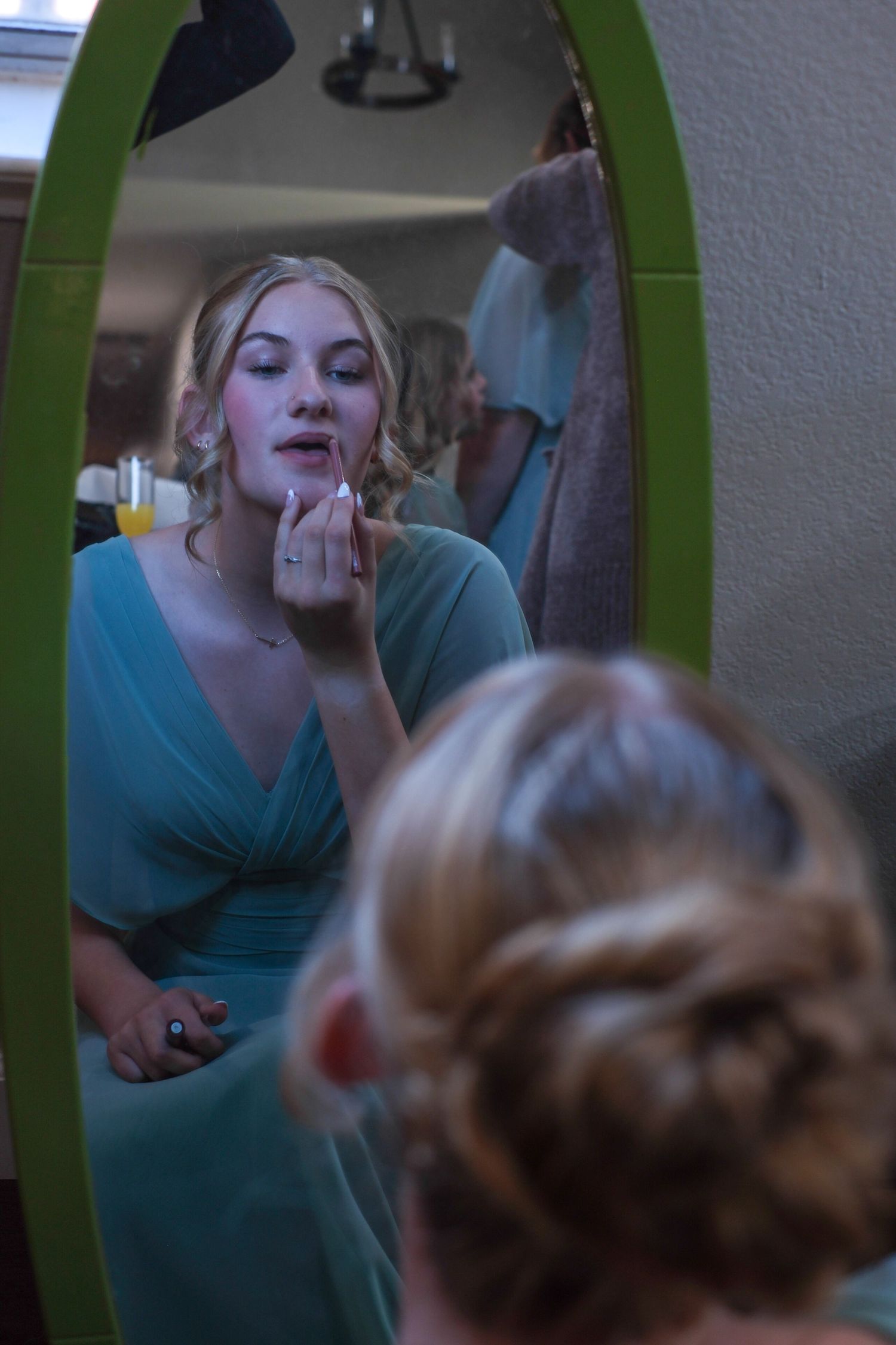 Sequence showing someone in a turquoise shirt applying makeup in front of a green framed mirror.