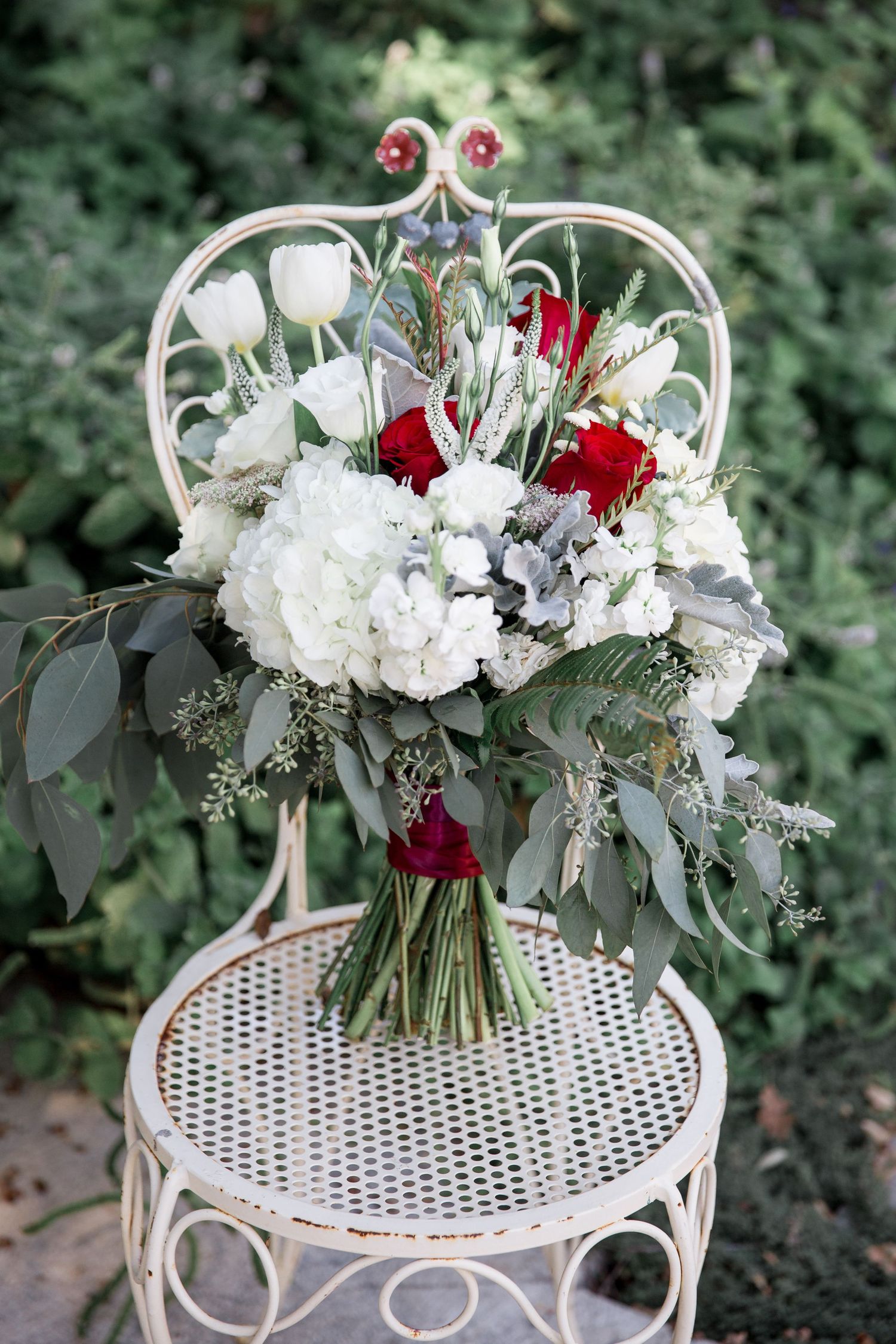Elegant floral arrangement of white hydrangeas and red roses displayed on a vintage white metal garden chair.