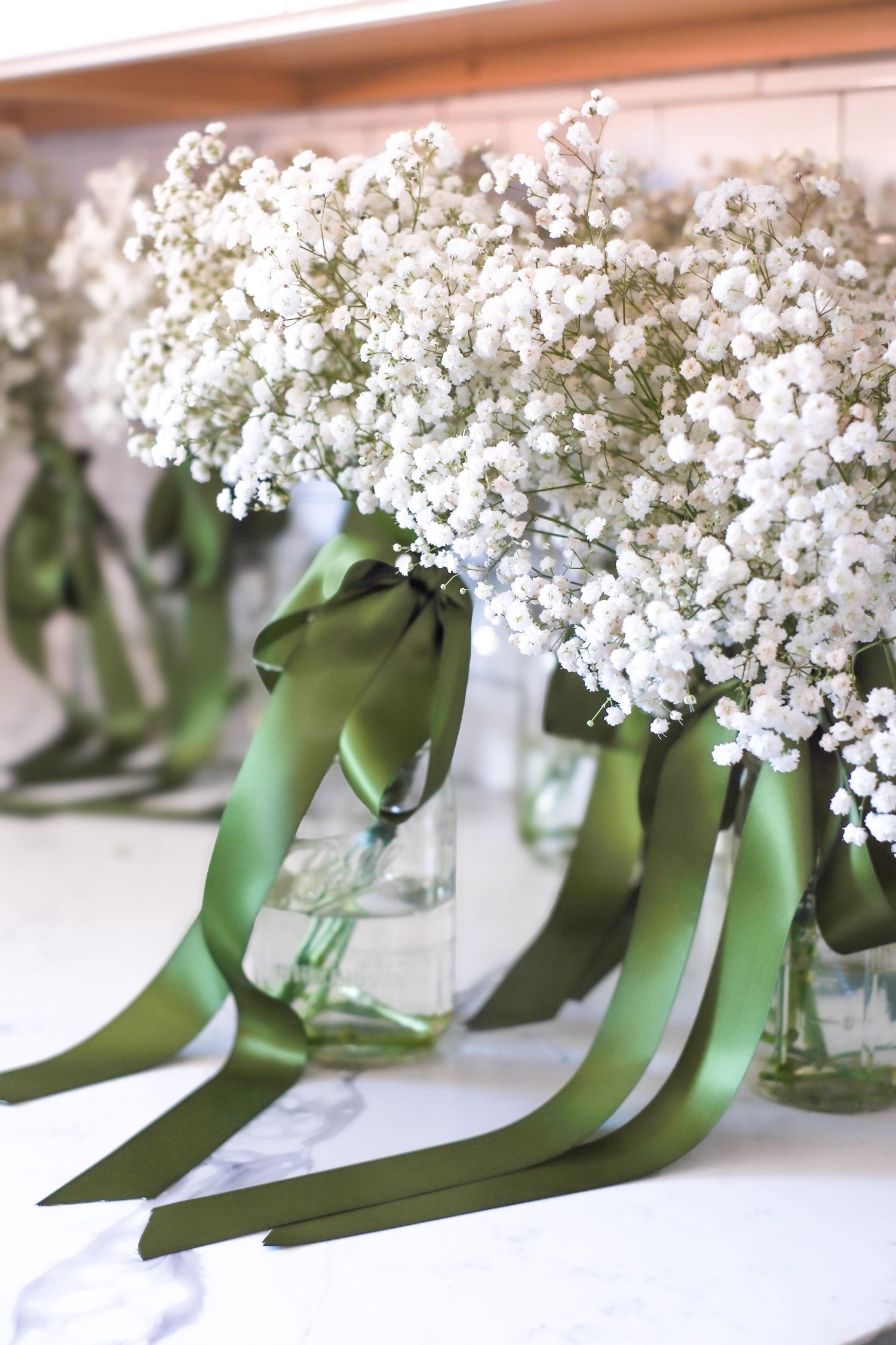 Glass vases filled with delicate white baby's breath flowers tied with elegant green satin ribbons arranged in a row.