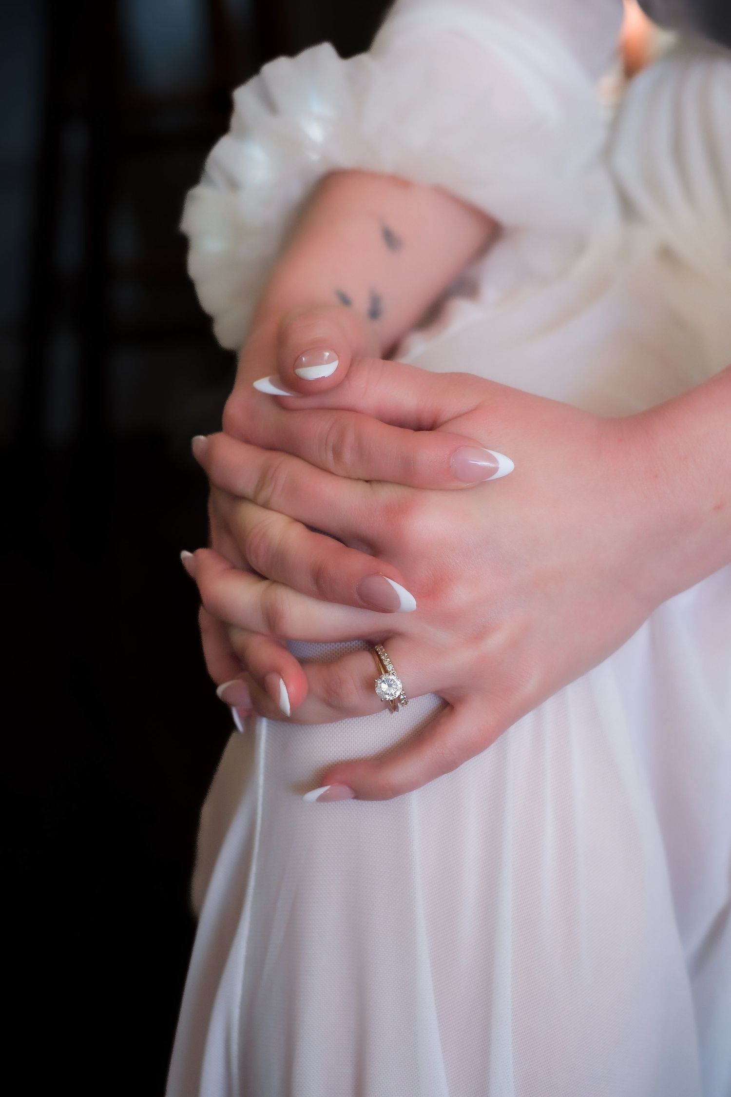 Hands with white manicured nails and an engagement ring gently hold flowing white fabric in a series of closeup shots.